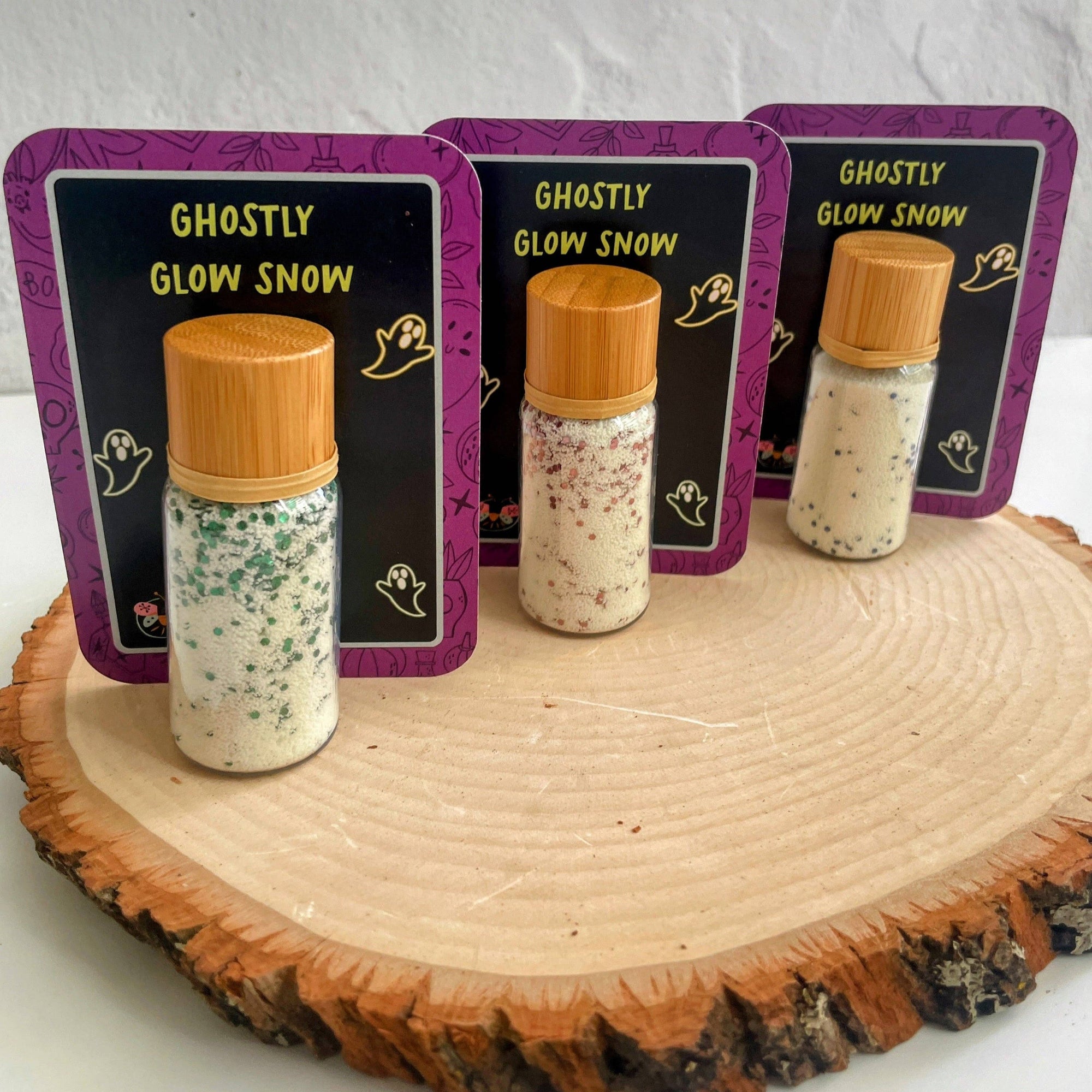 Three bottles of 'Ghostly Glow Snow' with decorative labels on a wooden surface.