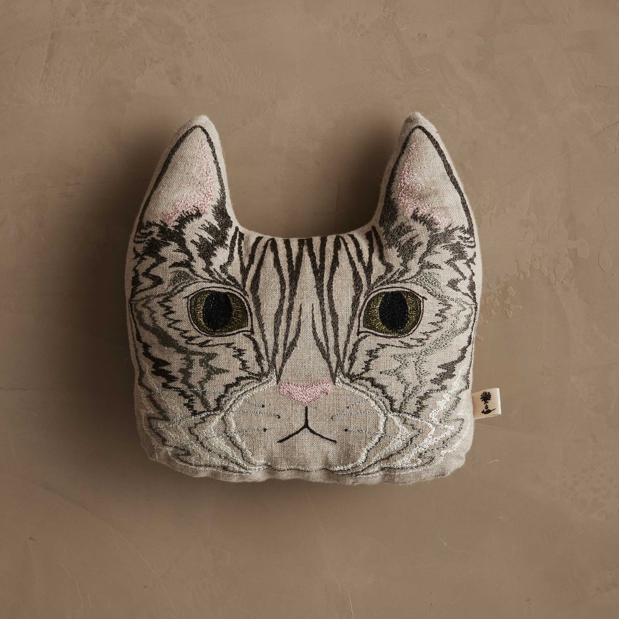 Cat-shaped pillow with embroidered face on a beige background