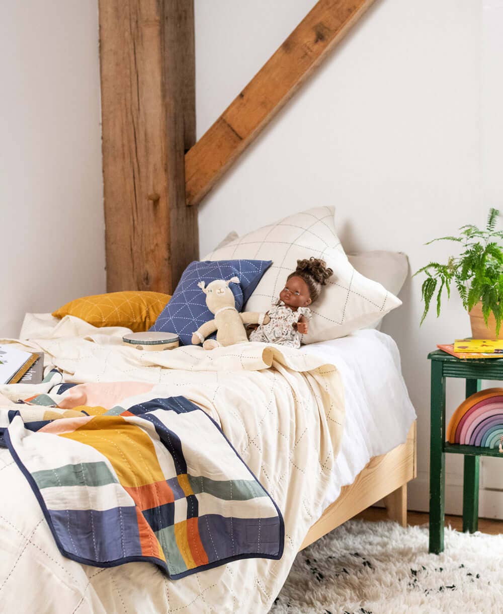 Child lying on a bed with colorful bedding and pillows in a cozy bedroom.