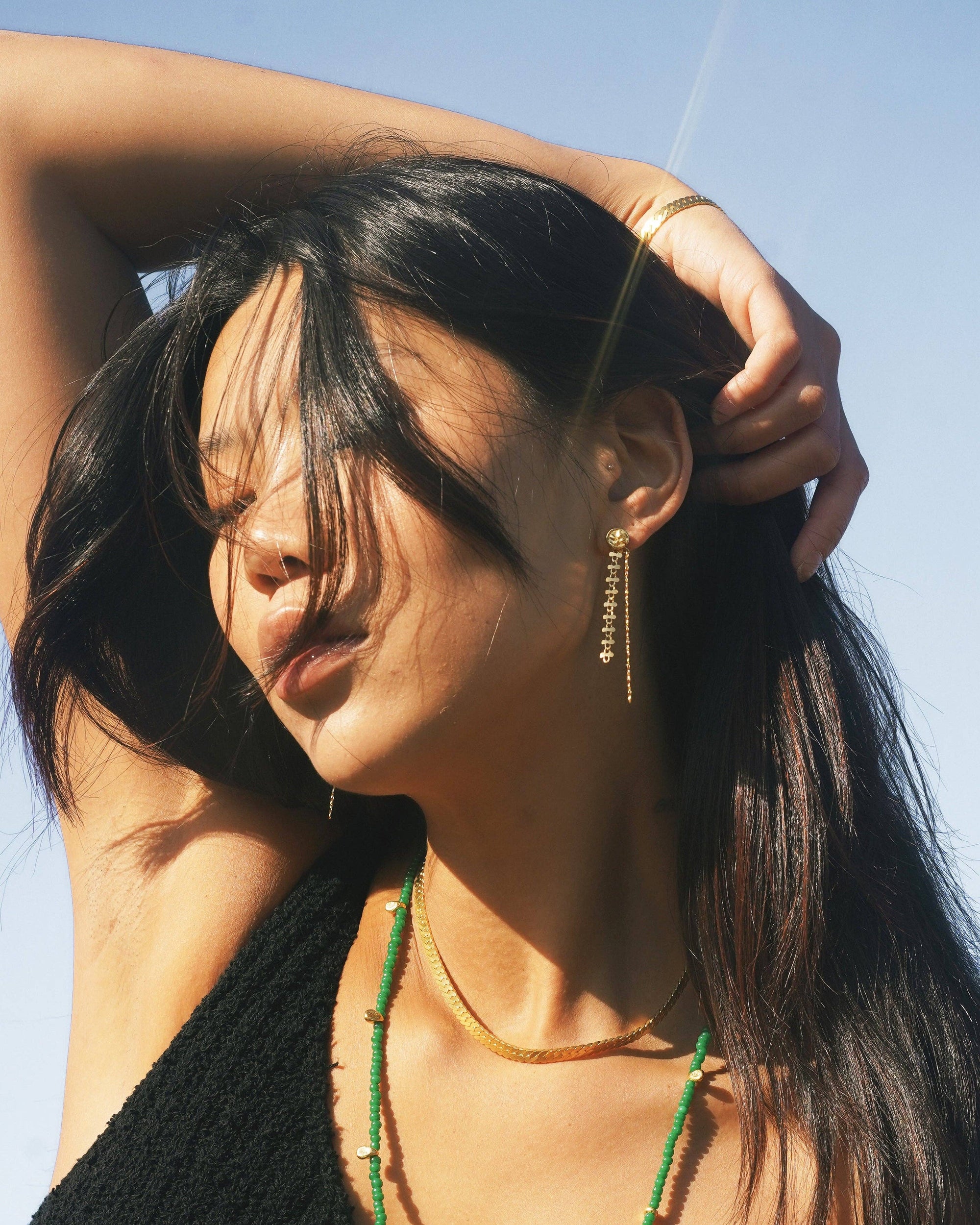 Woman with long dark hair and green necklace against a clear blue sky