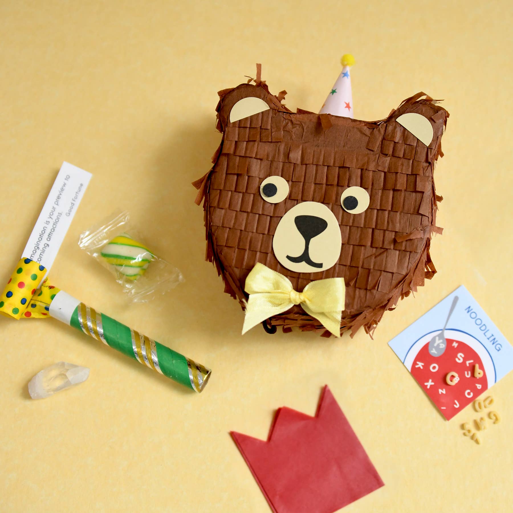 Brown bear-shaped piñata with a yellow bow on a yellow background