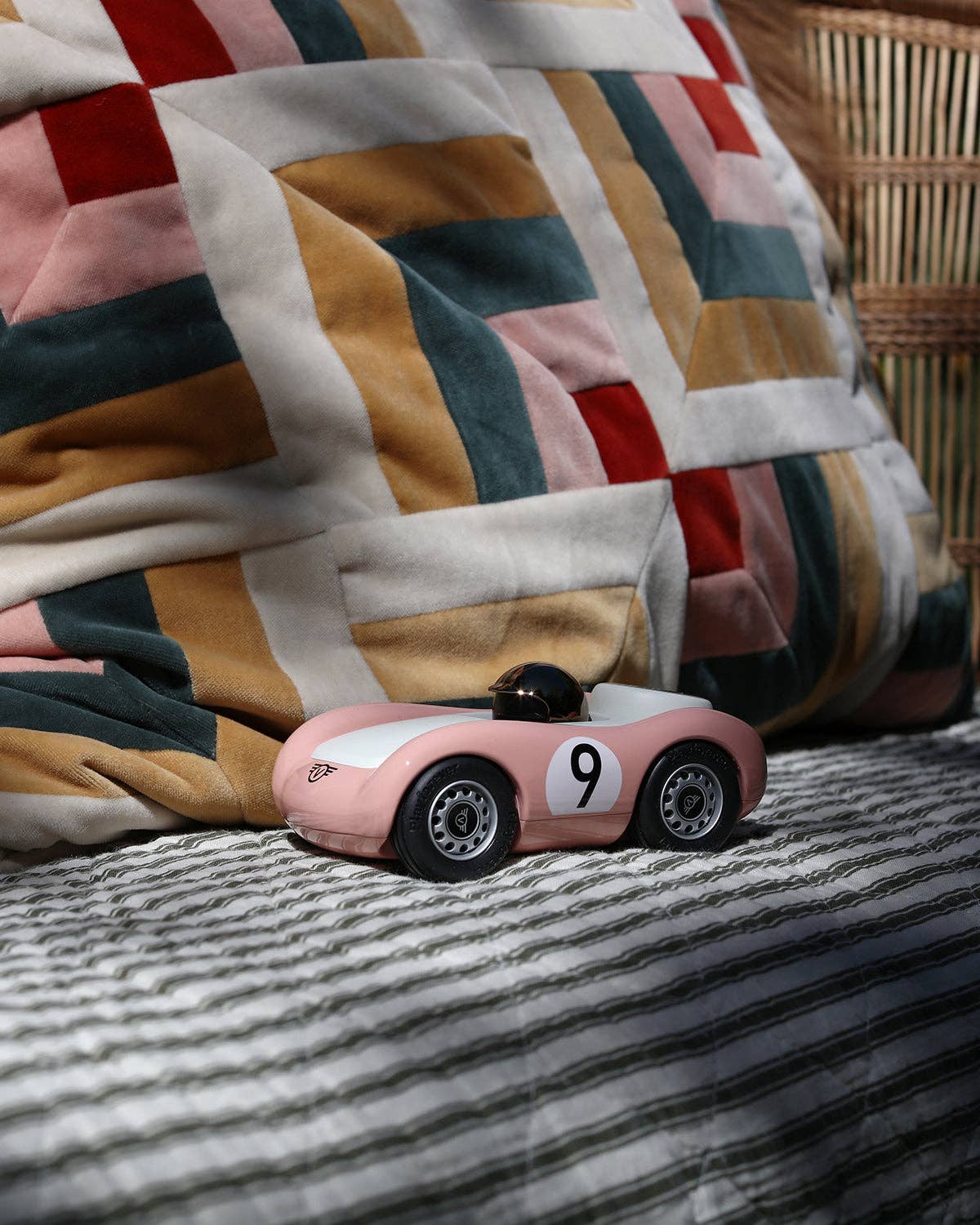 Pink toy car with number 9 on a striped fabric surface, with a quilted blanket in the background.