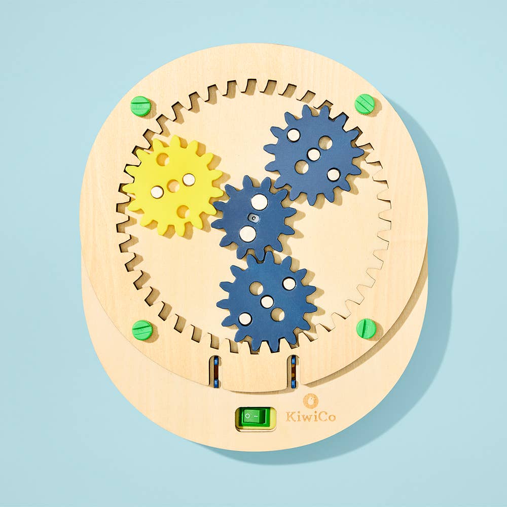 Wooden gear mechanism with blue and yellow gears on a light blue background, branded 'KiwiCo'.