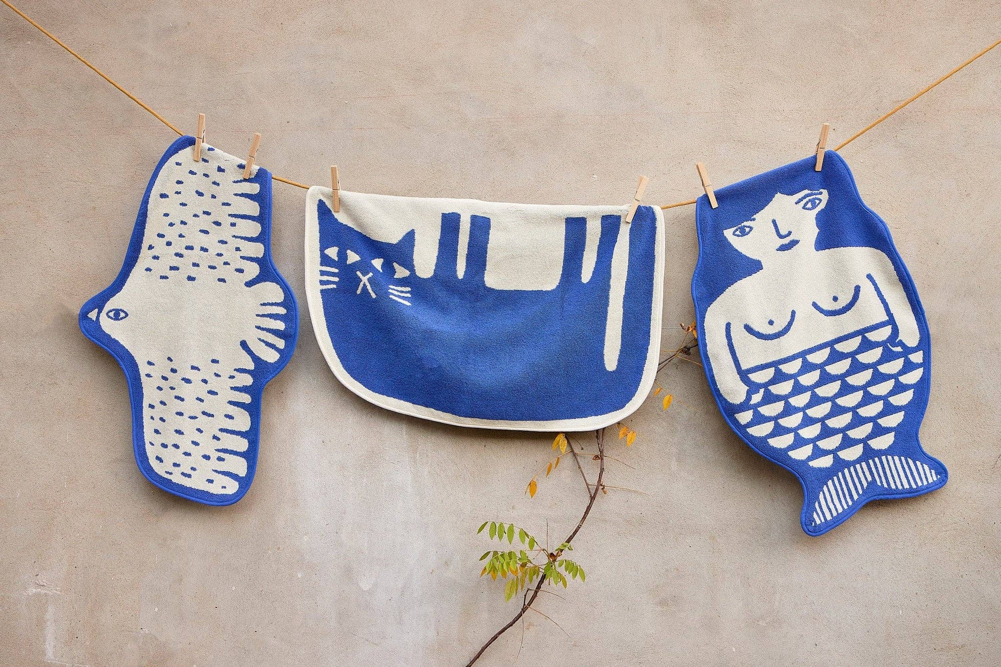 Three blue and white ceramic plates shaped like animals hanging on a line against a beige wall.