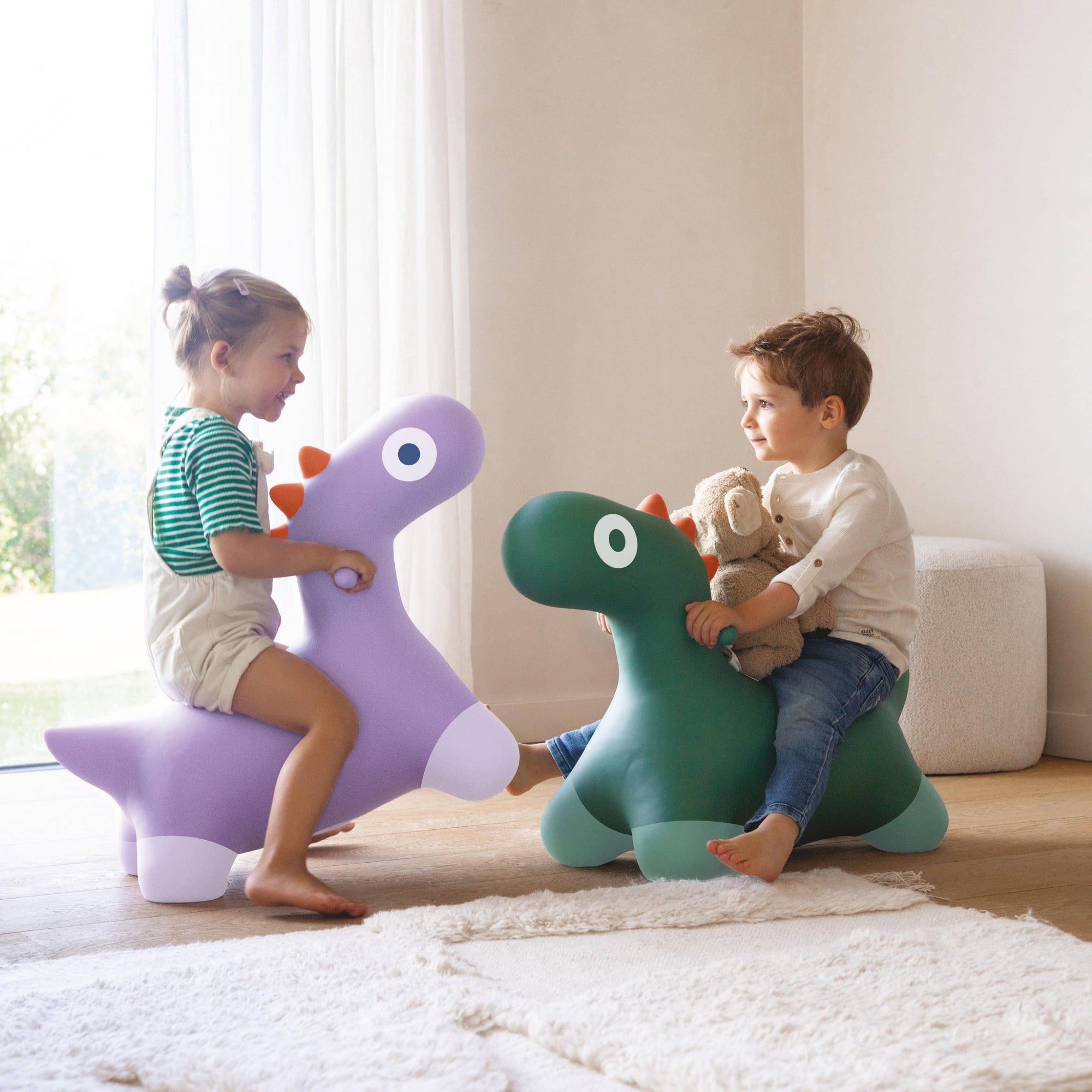 Two children playing with dinosaur-shaped toys in a bright room.