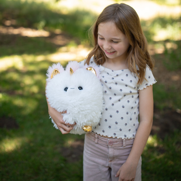 Young girl holding a fluffy white toy with gold accents outdoors.