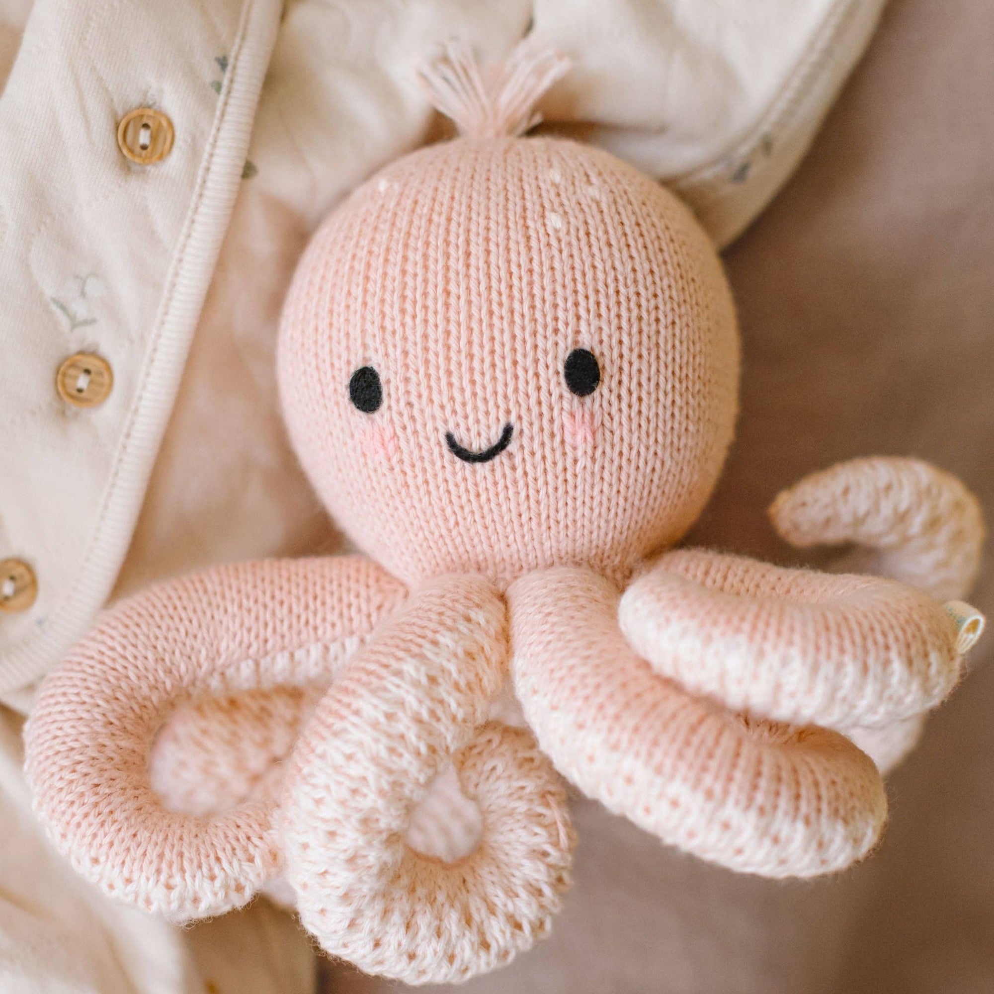 Knitted octopus toy with a smiling face held by a person wearing a light-colored jacket.