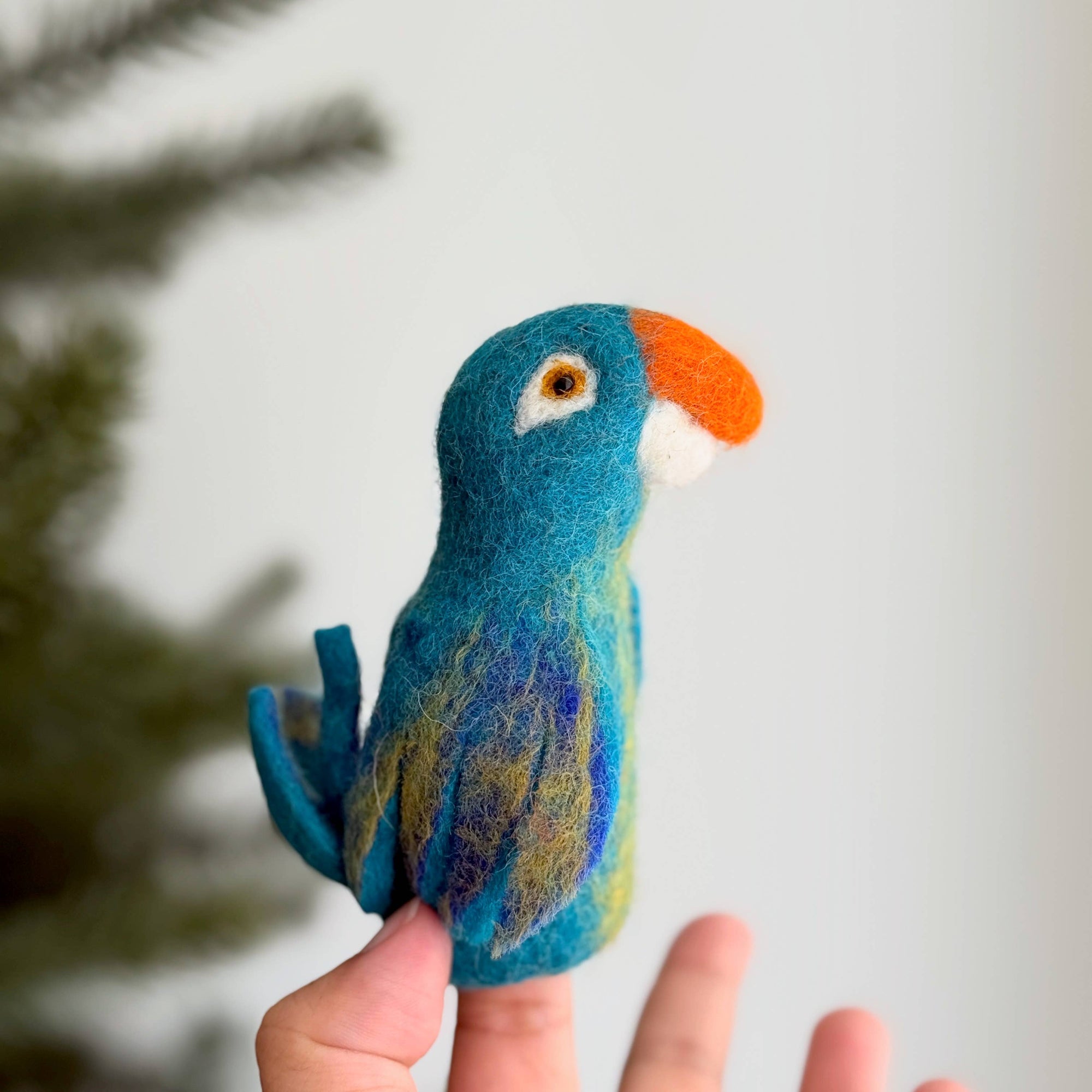 Hand holding a felted parrot toy against a blurred natural background