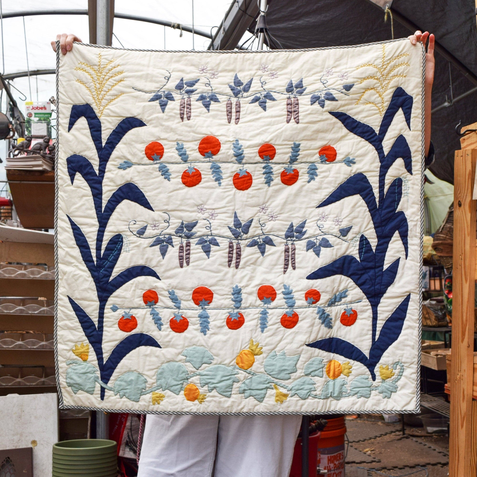 Person holding a quilt with floral patterns in blue, red, and orange on a white background.