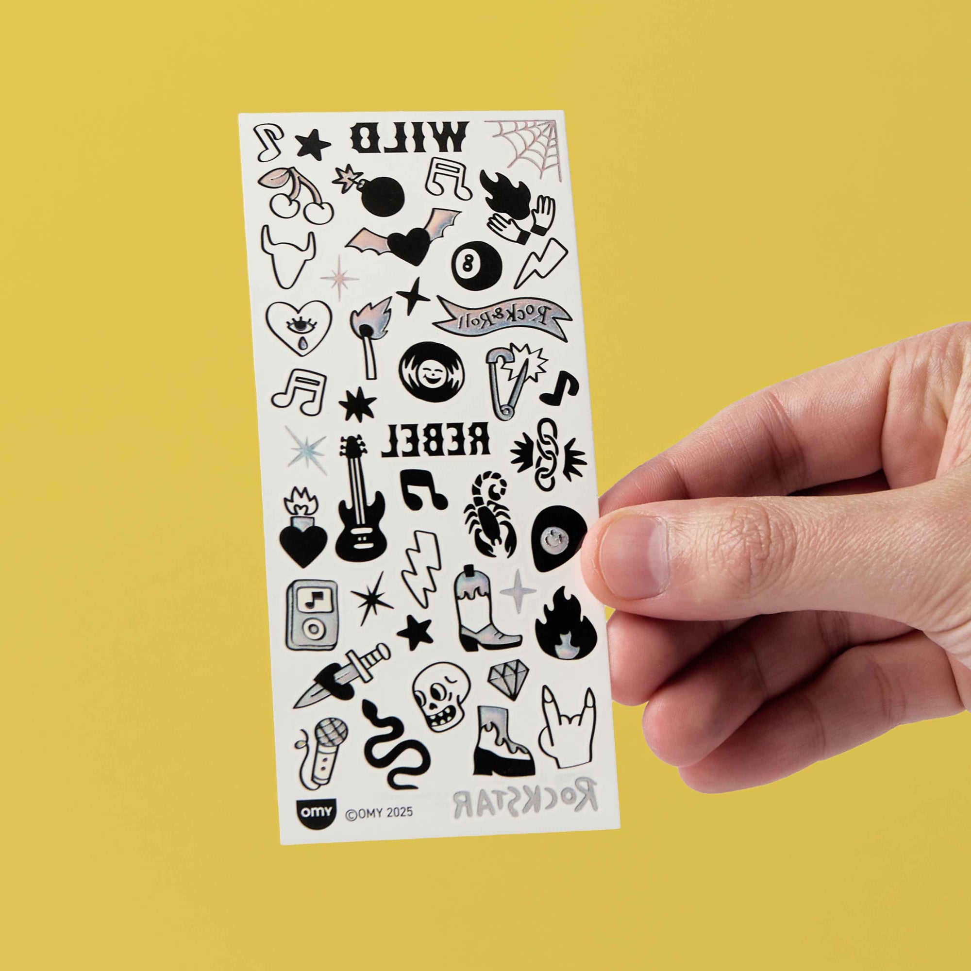 Sheet of black and white temporary tattoos held by a hand against a yellow background
