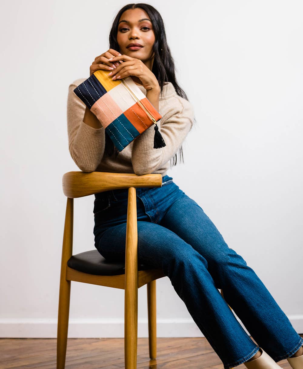 Woman sitting on a wooden chair holding a colorful striped blanket against a white wall.