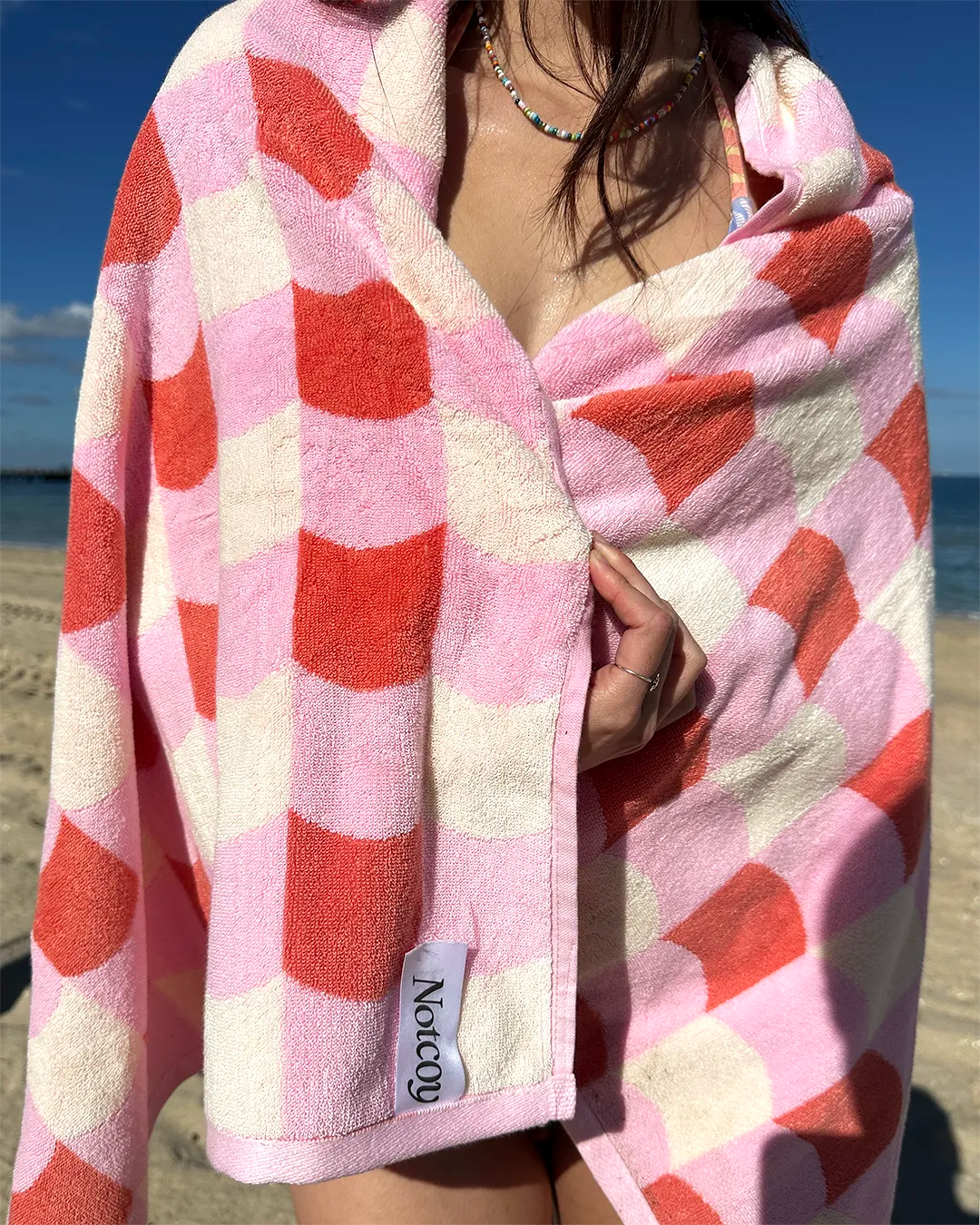 Person wrapped in a pink and red checkered towel on a beach