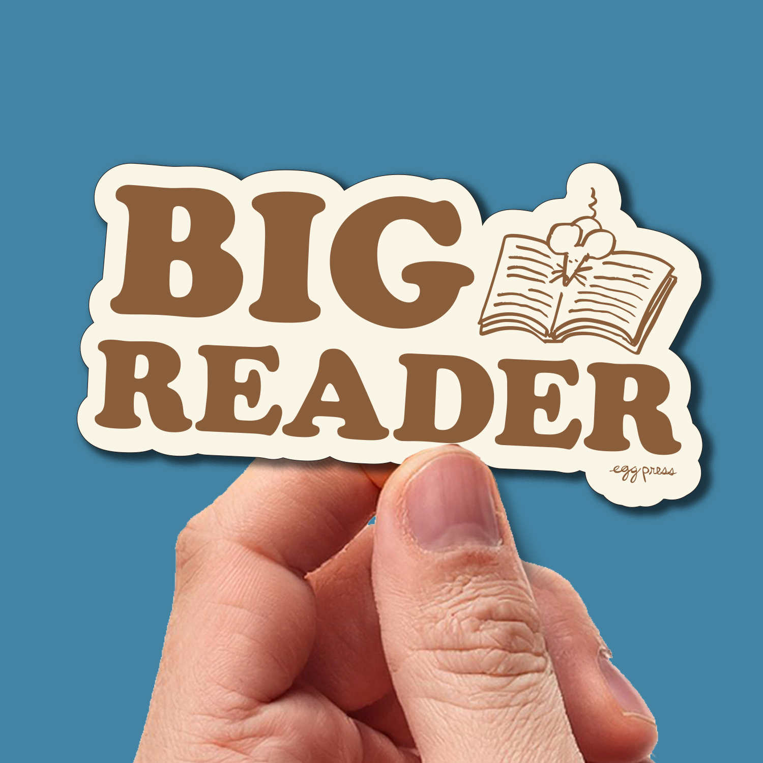Sticker with 'BIG READER' text held by a hand against a blue background