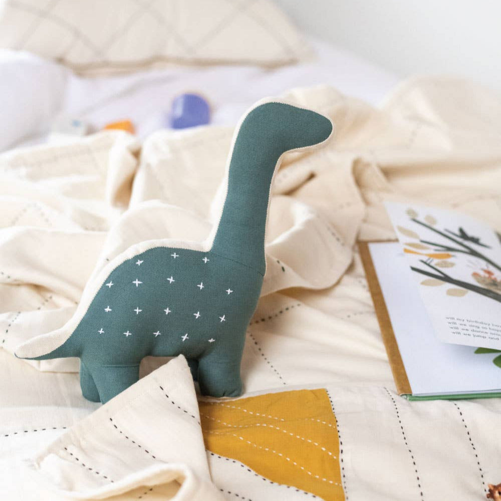 Green dinosaur plush toy on a quilted surface with a magazine in the background