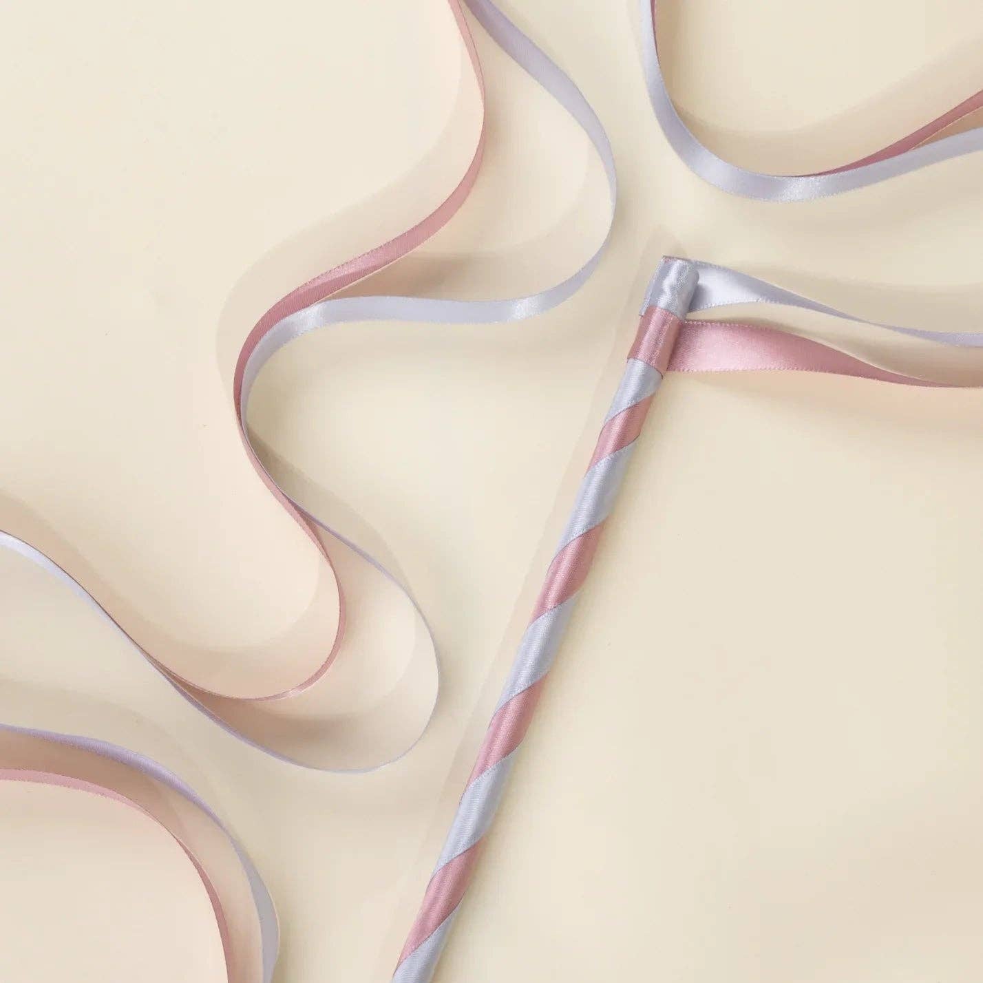 A pastel pink and light blue striped wand r with matching ribbon tails, laid diagonally on a warm cream background.