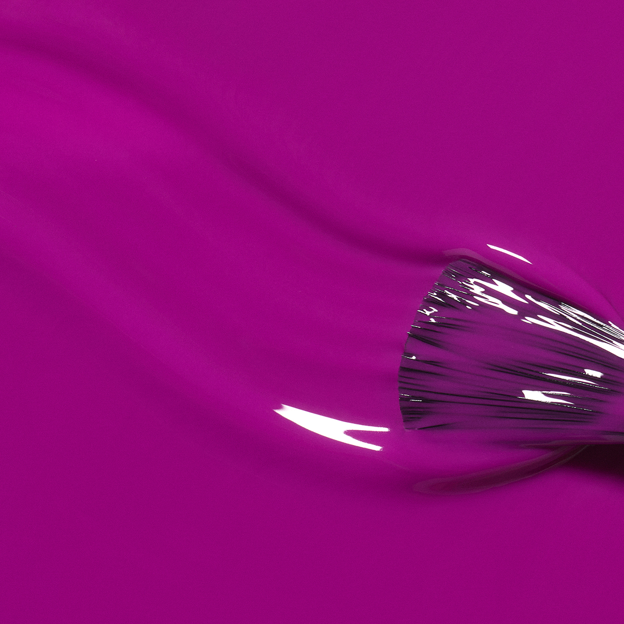 A close-up of glossy bright magenta nail polish with a brush stroke on the right side, showing the translucent finish and bristles against a matching colored background.