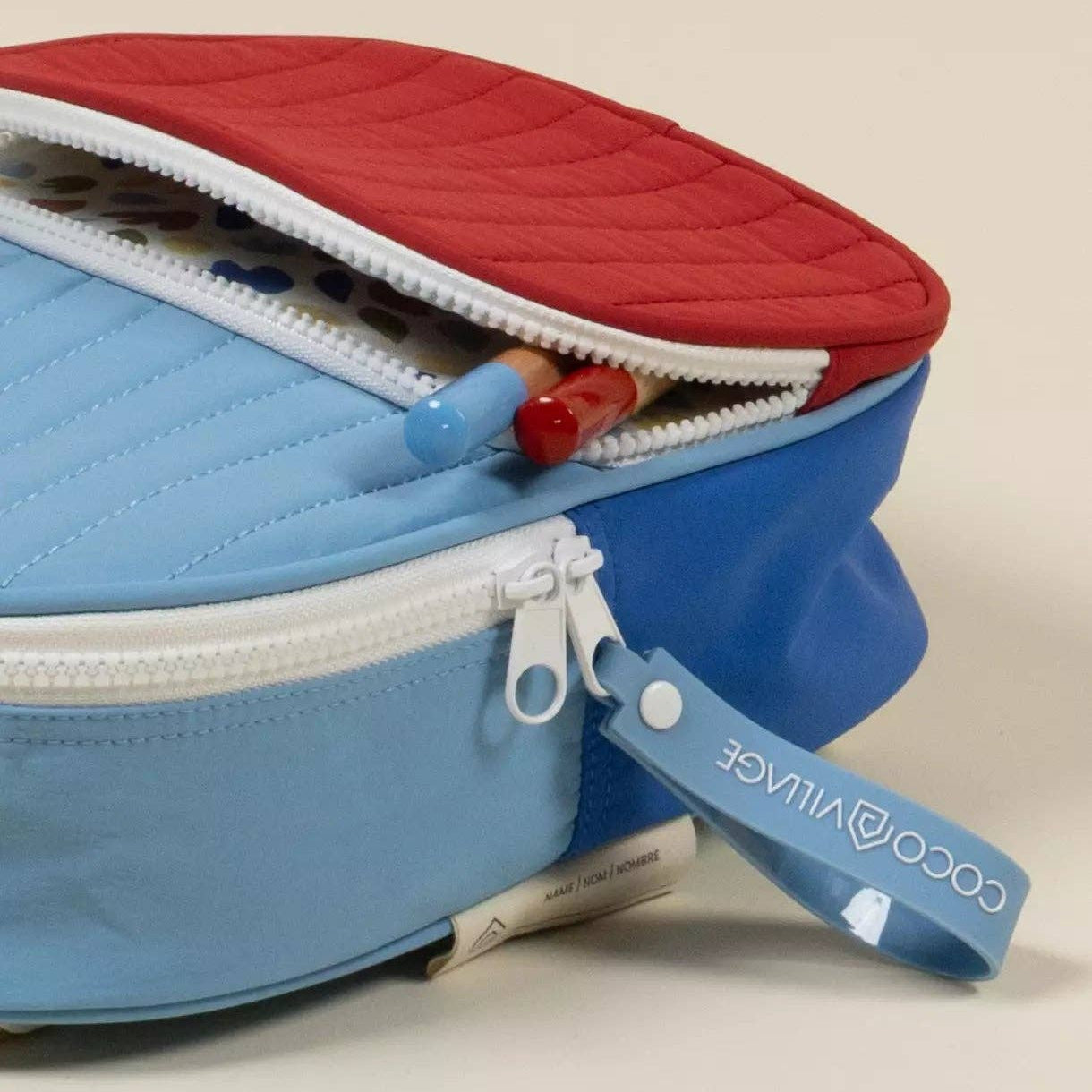Blue and red pencil case with a visible brand label on a beige background