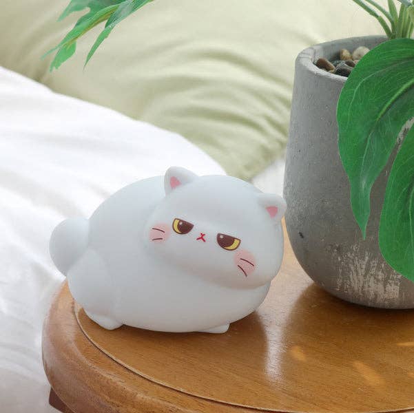 White cat-shaped night light on a wooden surface with a plant in the background
