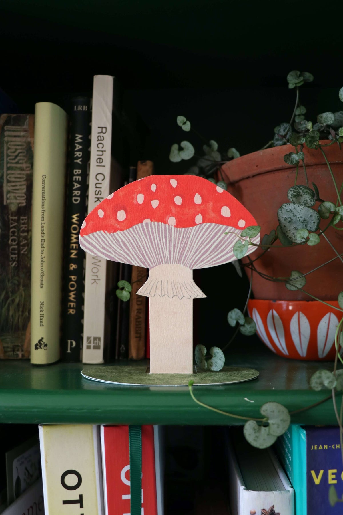 Wooden mushroom decor on a bookshelf with books and plants in the background