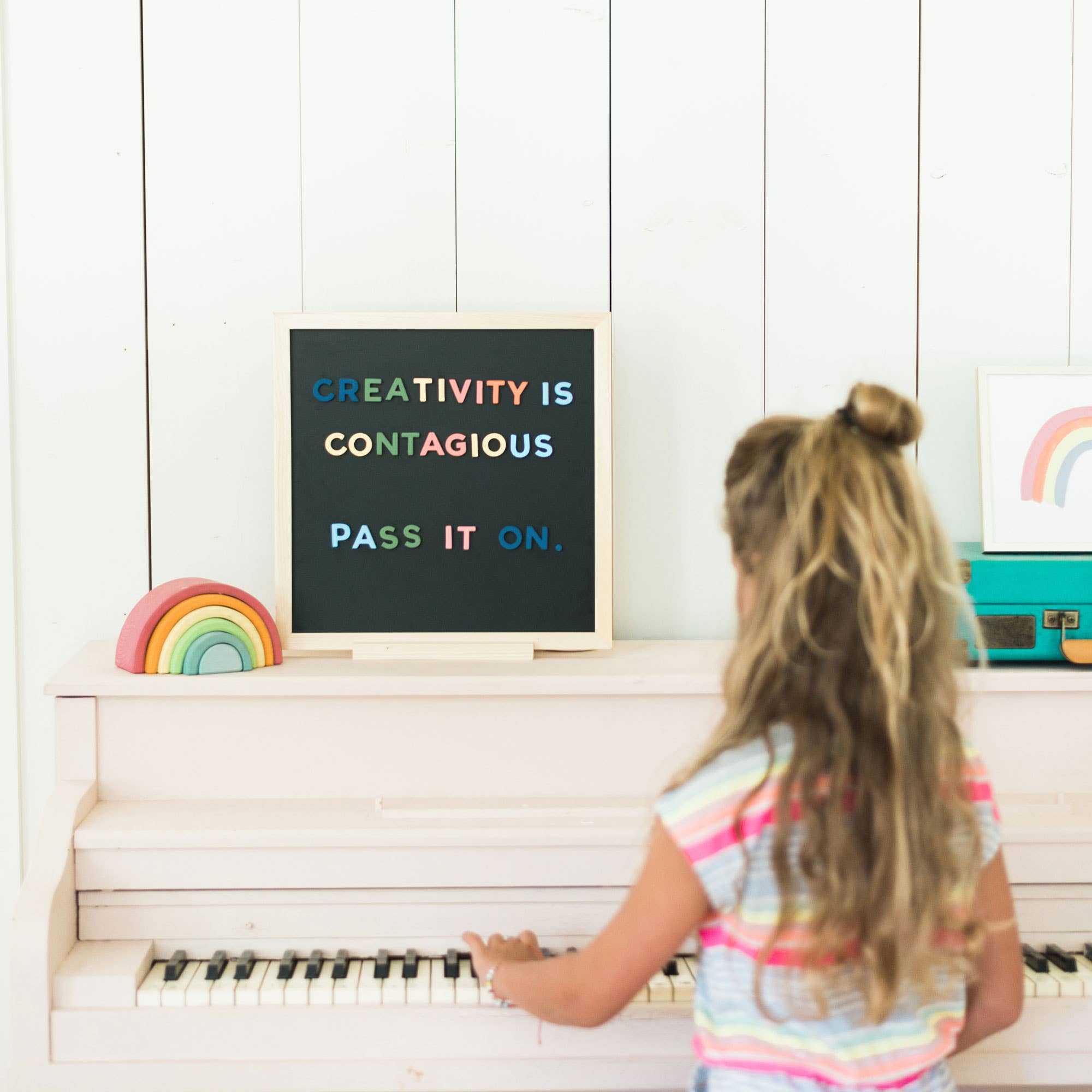 Child playing piano with 'Creativity is Contagious' sign on white wall