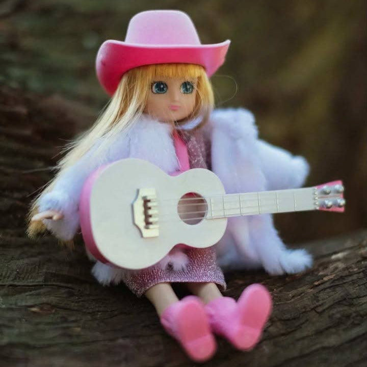 Doll in a cowboy outfit with a pink hat, white coat, and pink boots sitting on a wooden surface.