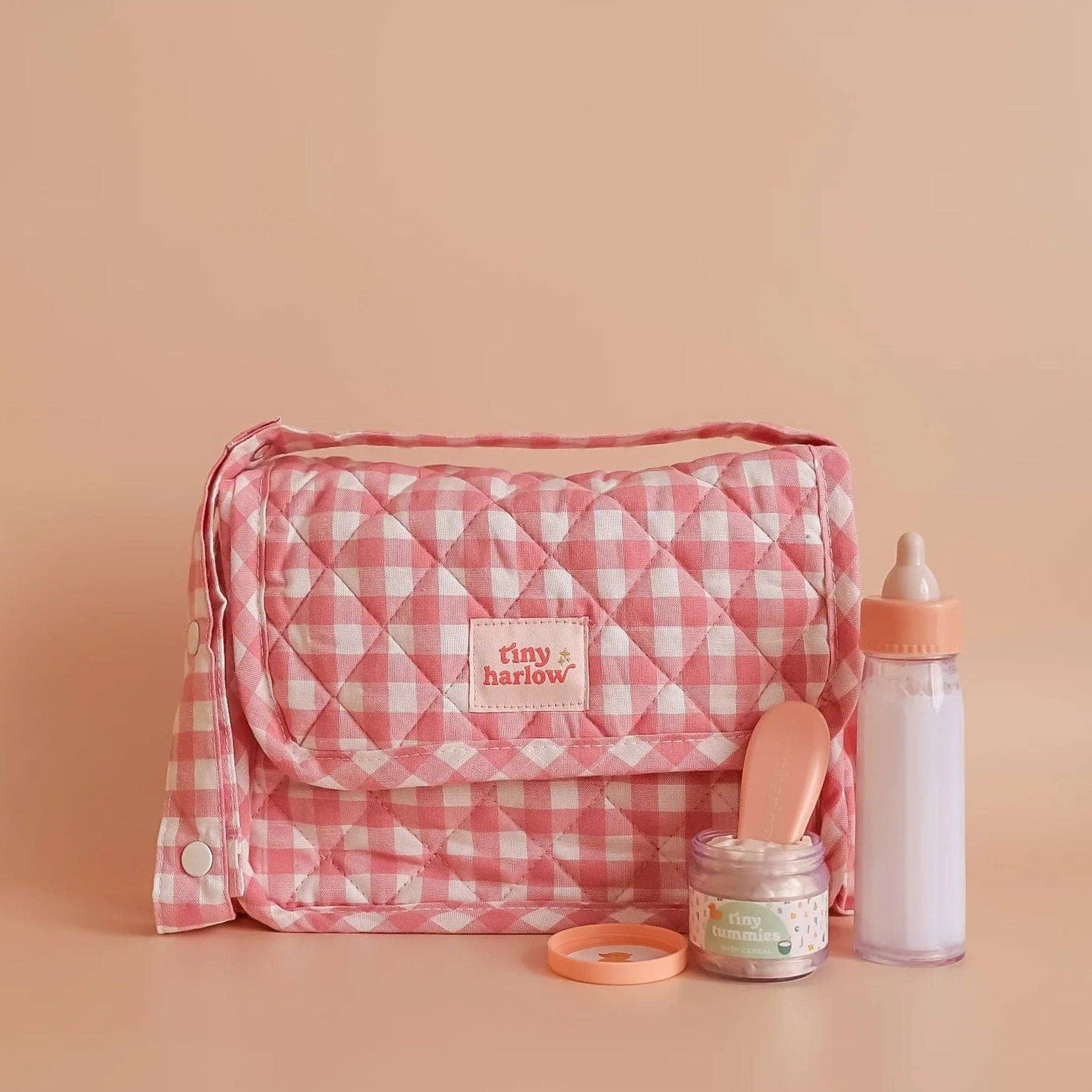 Pink gingham bag with baby care items on a beige background