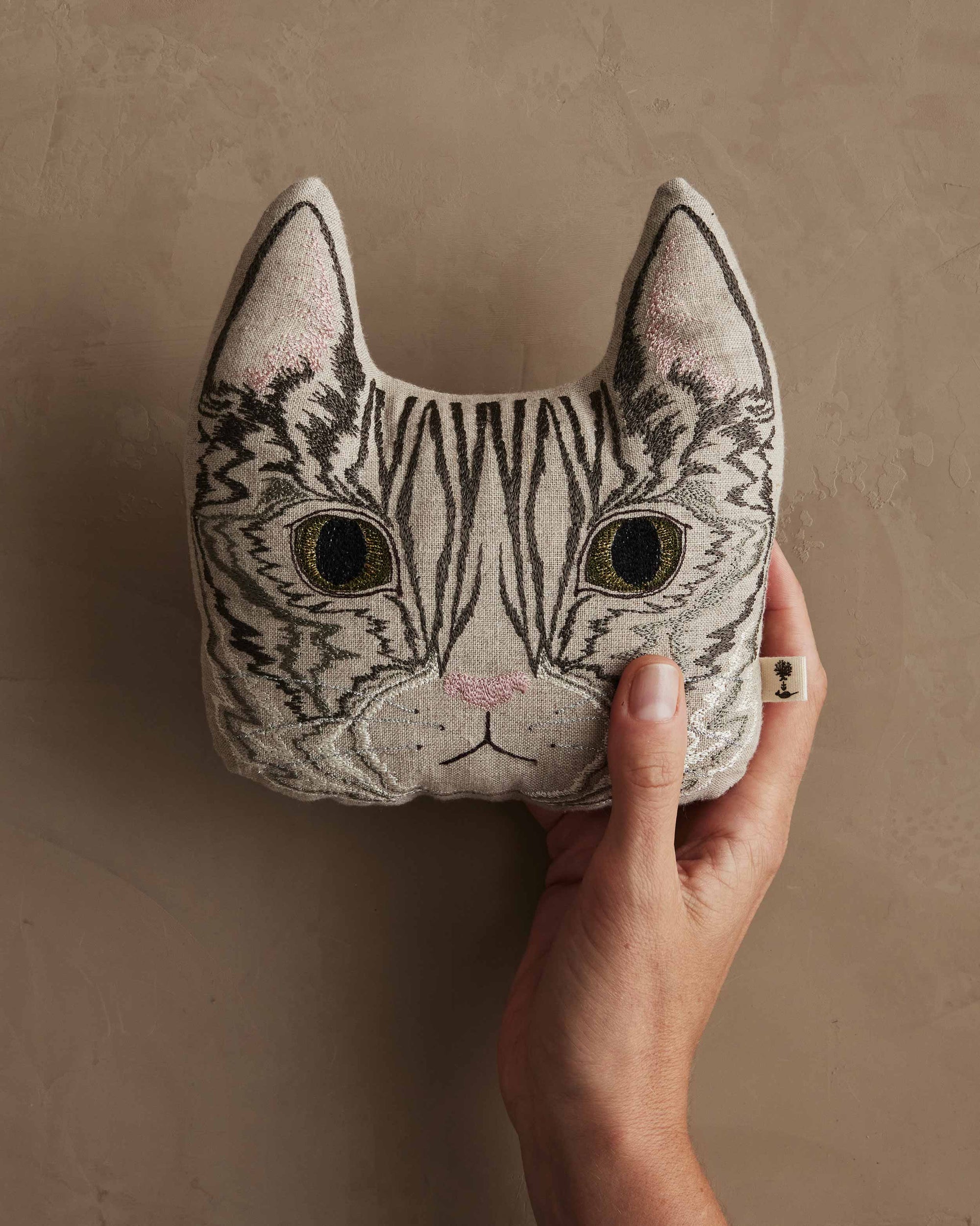 Hand holding a cat-shaped plush toy against a beige background