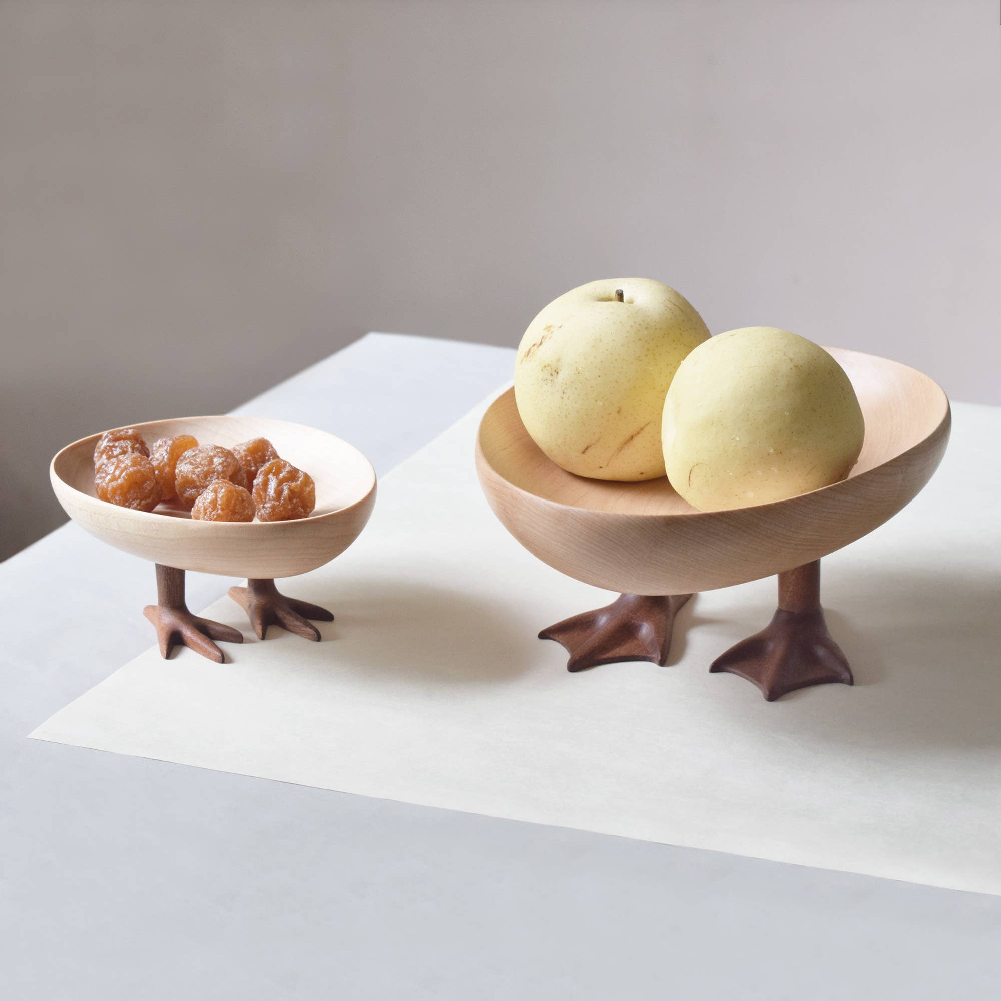 Two wooden bowls with bird-like legs on a light surface