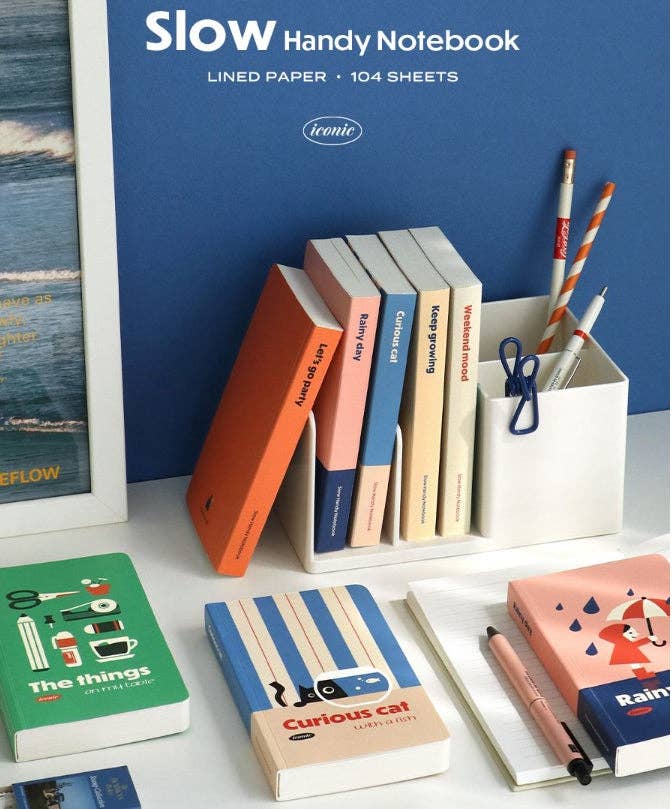 Collection of notebooks and stationery items with a 'Slow Handy Notebook' in the background.