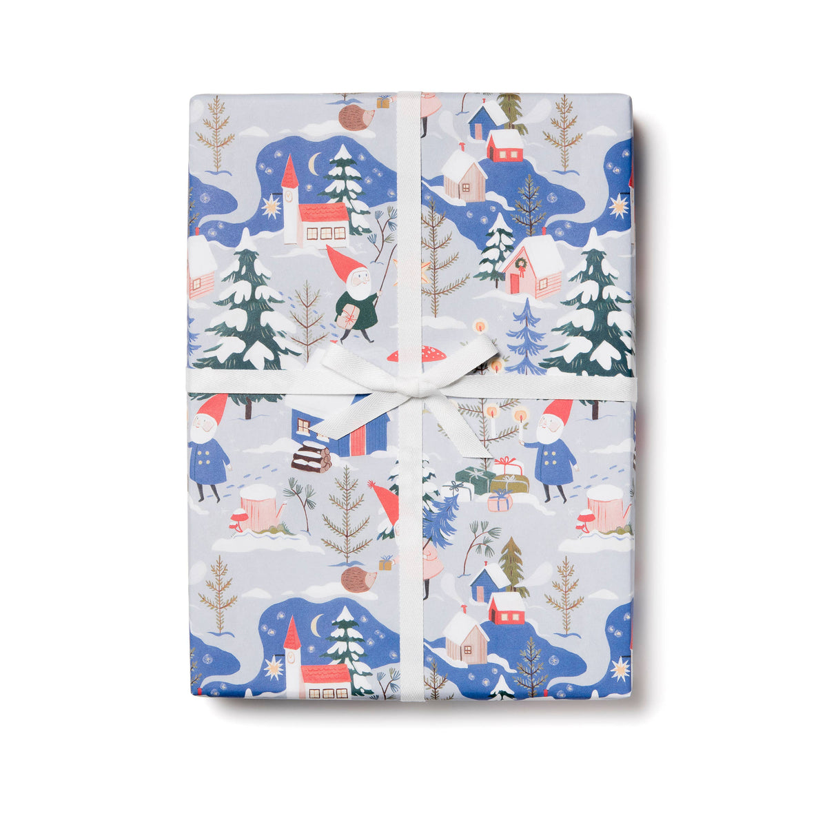 A gift-wrapped rectangular box tied with a white ribbon, featuring a winter village print with blue snowy hills, evergreen trees, small houses, and figures in red hats, on a white background.