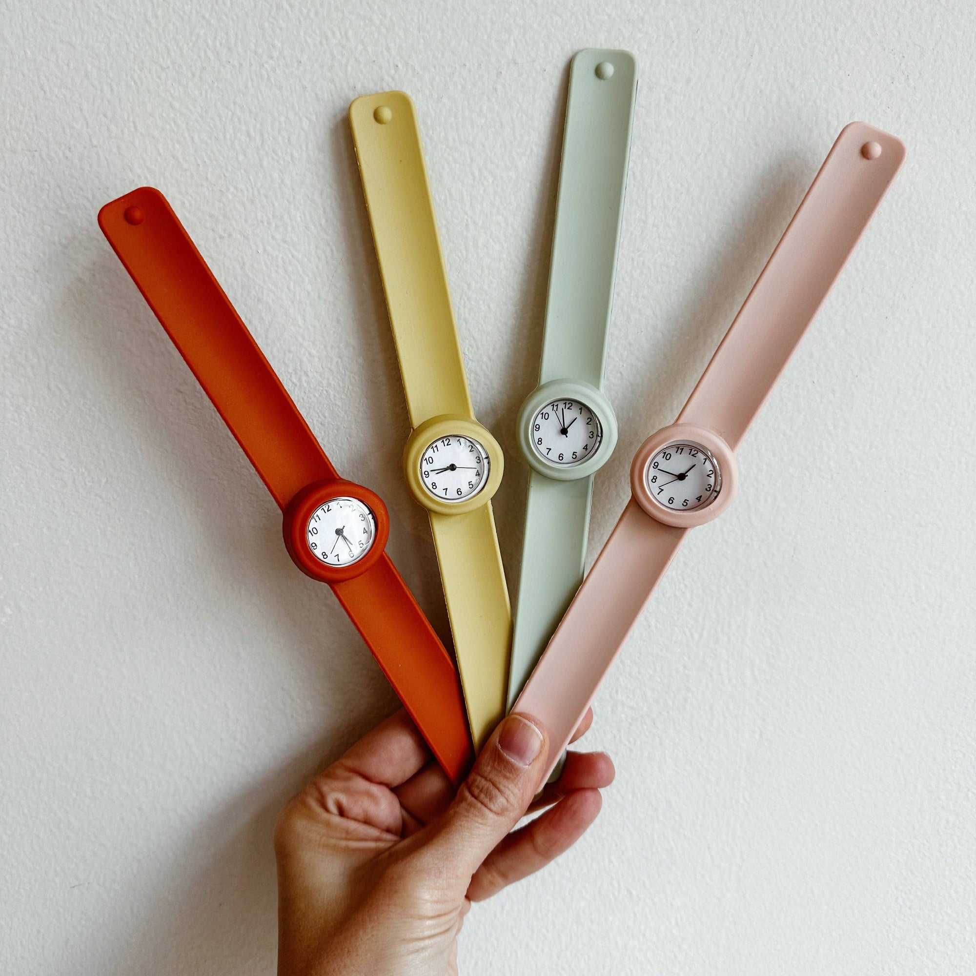 Four colorful wristwatches held by a hand against a light background