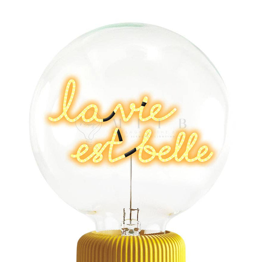 Neon light bulb with 'la vie est belle' text on a yellow ribbed base against a white background