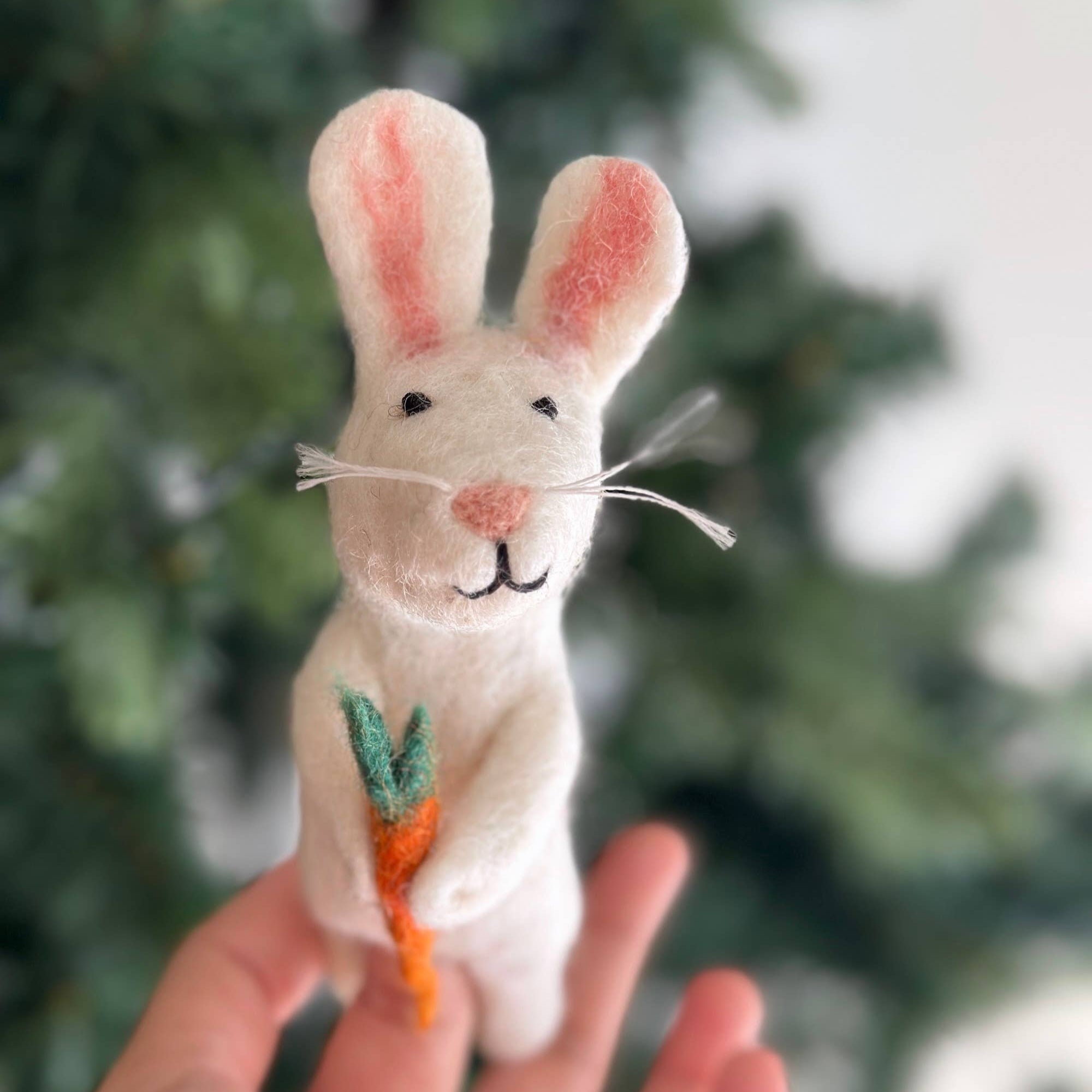 Felted rabbit toy held in a hand with a blurred green and white background