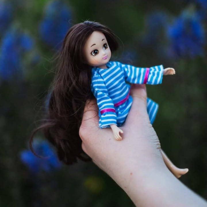 Hand holding a small doll with a striped shirt against a blurred natural background