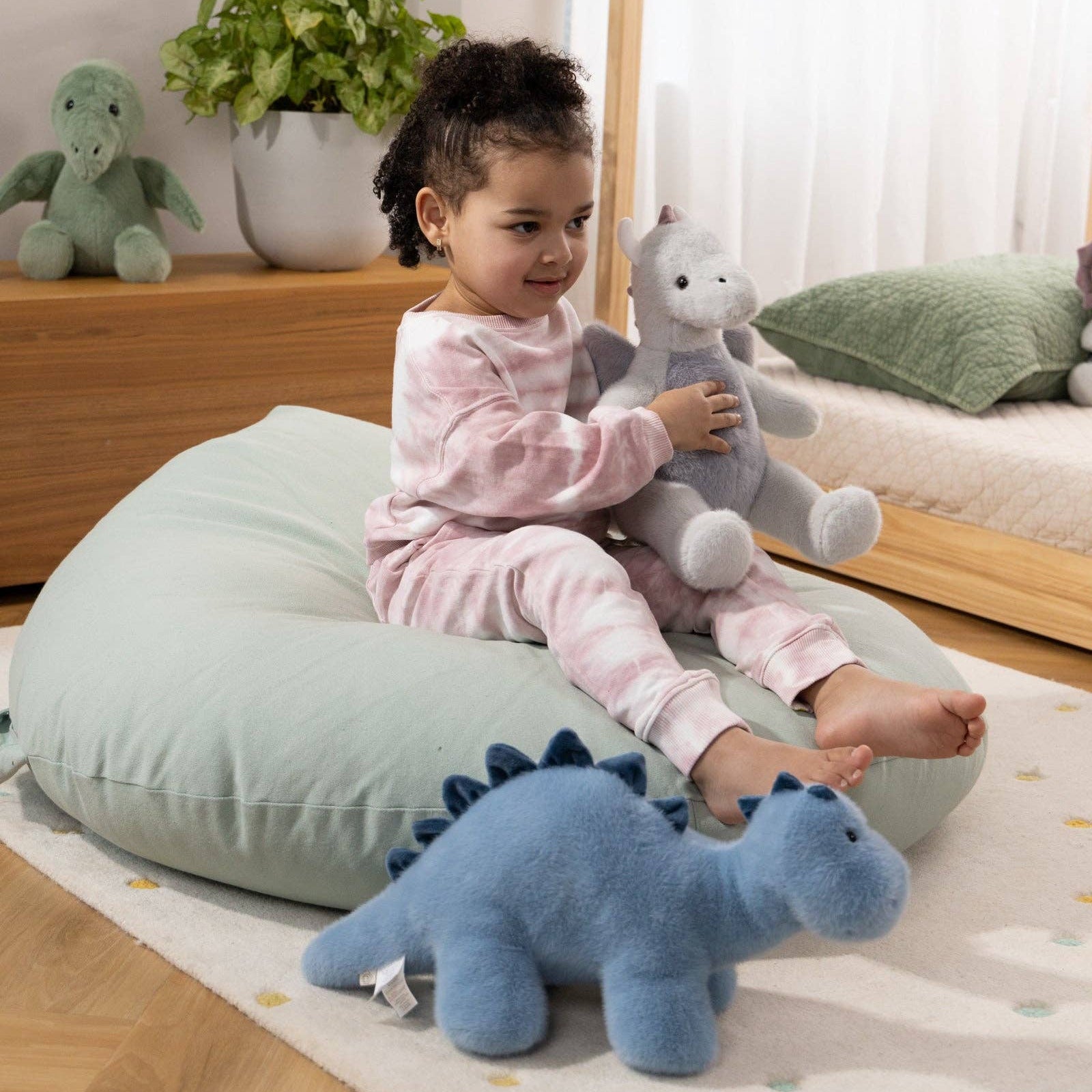 Child playing with stuffed animals on a soft surface in a home setting
