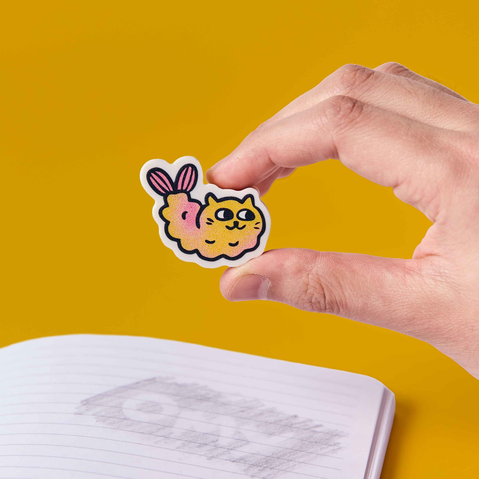 Hand holding a cartoon cat sticker with bunny ears on a yellow background