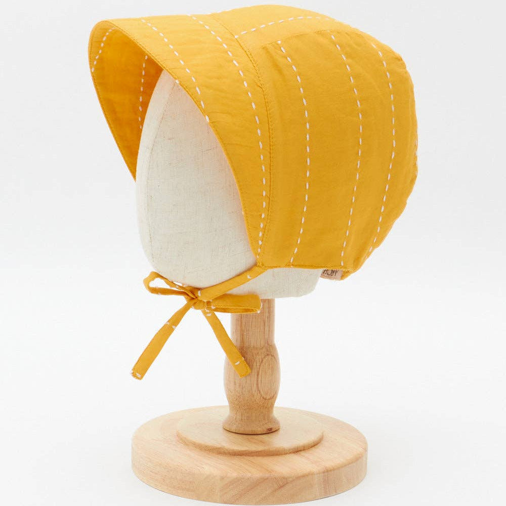Yellow baby bonnet on a wooden mannequin head against a white background