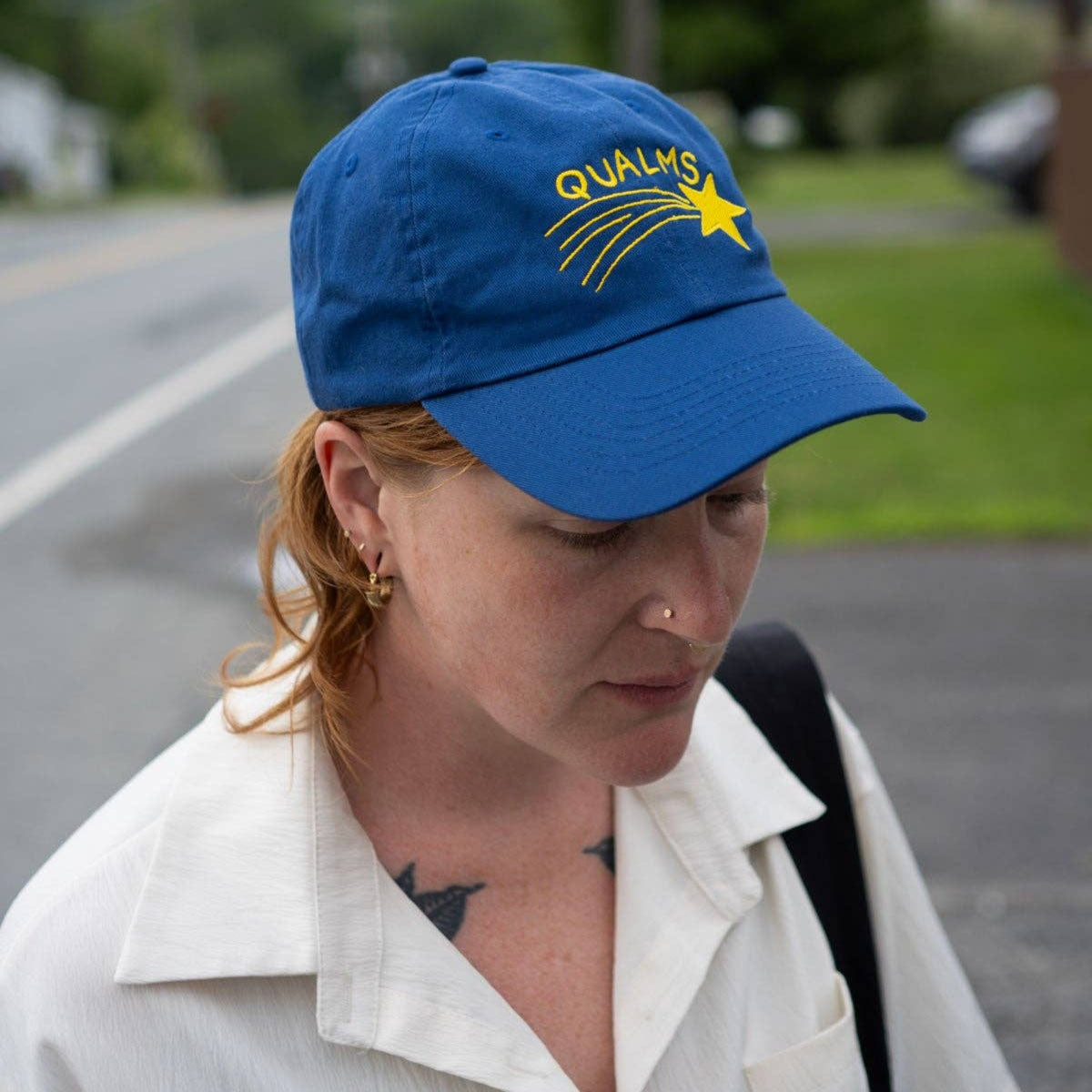 Person wearing a blue cap with a logo, standing outdoors on a road.