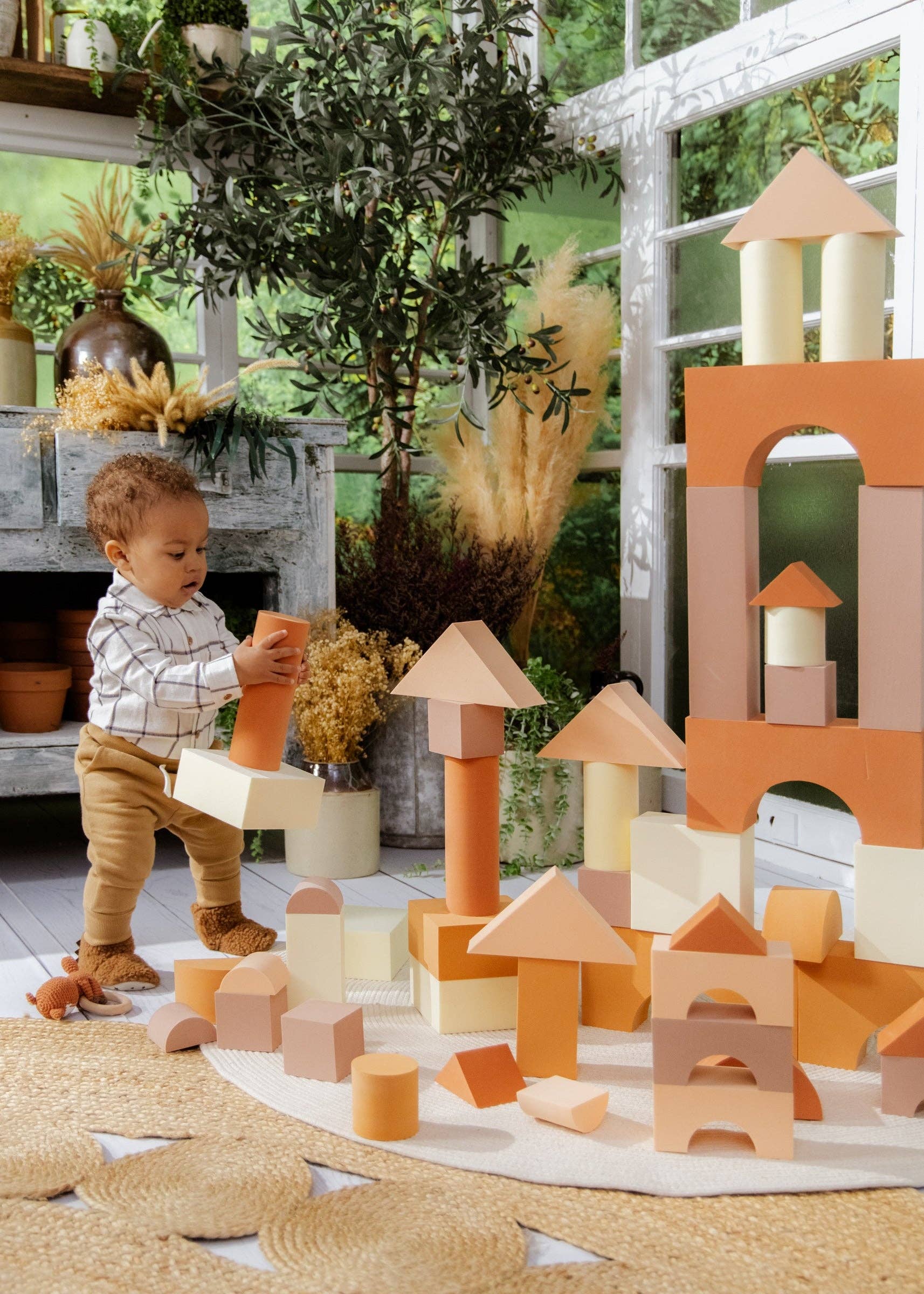 Child playing with wooden blocks in a sunlit room with plants and a fireplace.