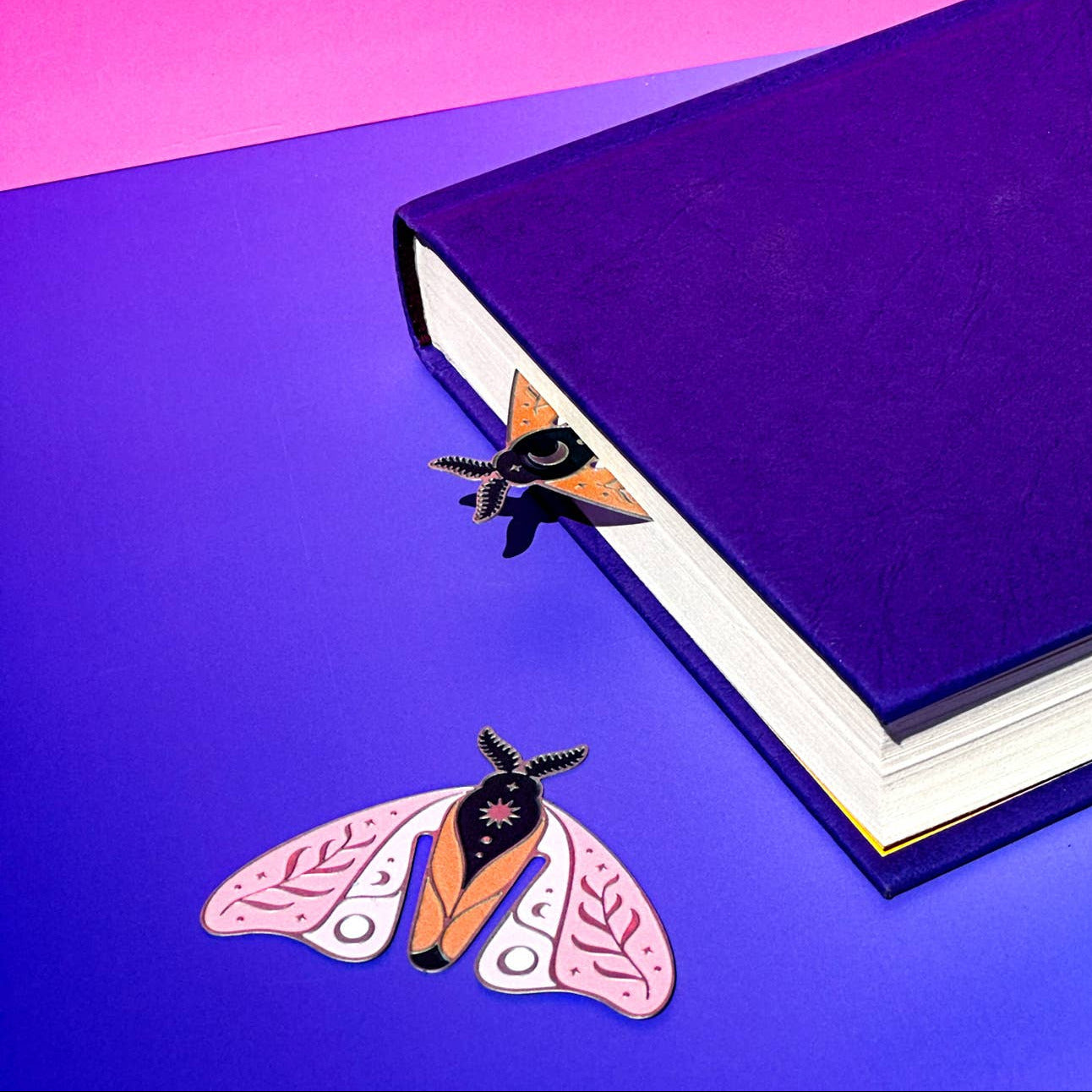 Two butterfly-shaped pins on a purple surface with an open book in the background.