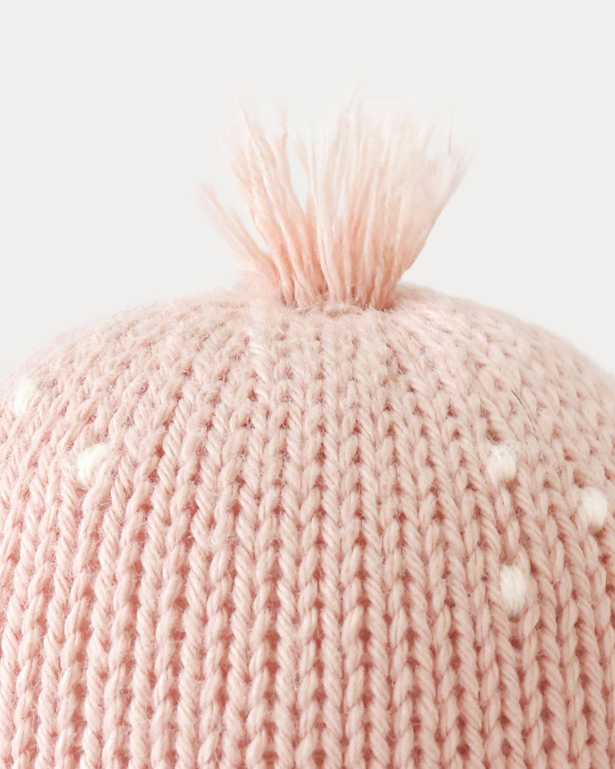 Close-up of a pink knitted beanie with a fluffy pom-pom on a light gray background