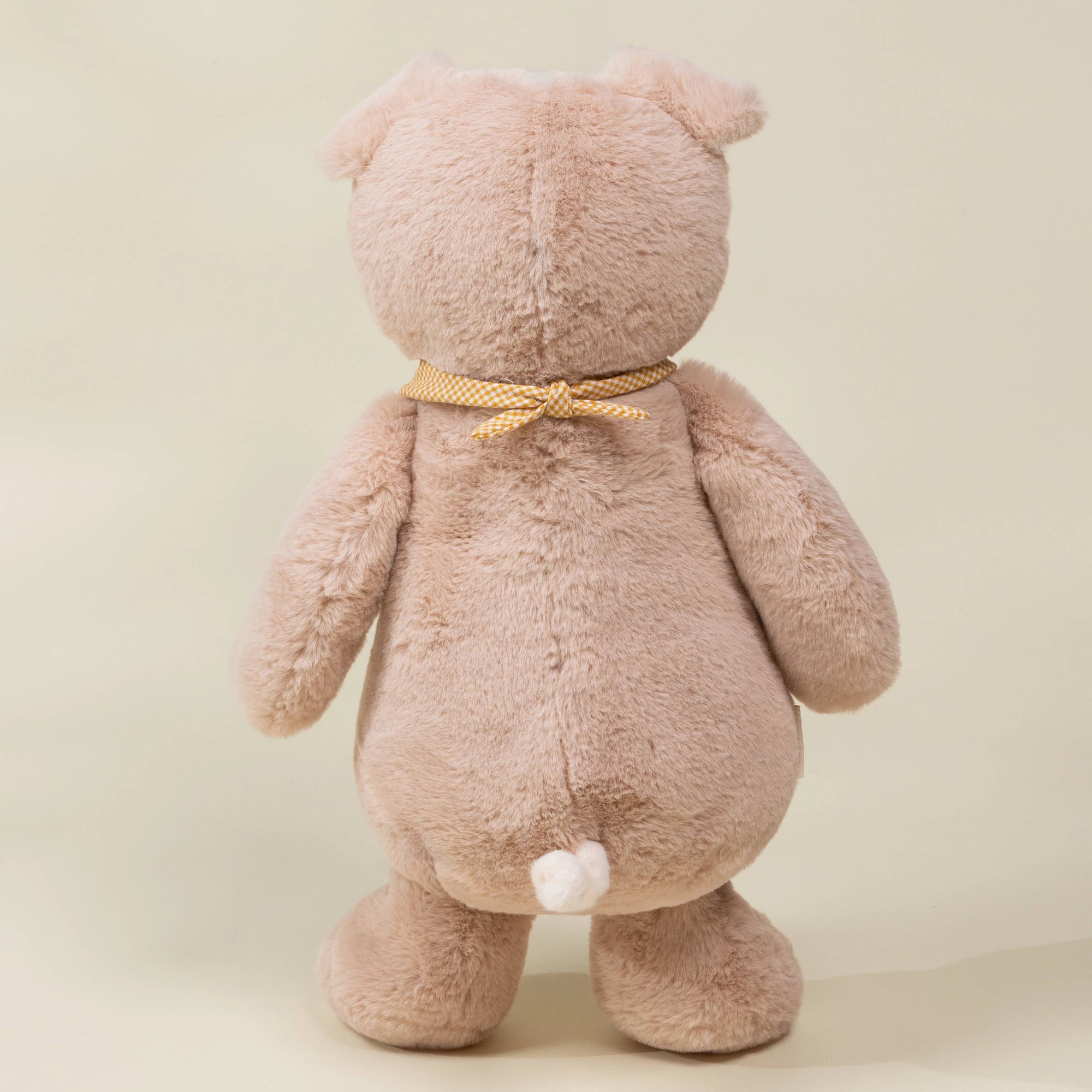 Back view of a plush teddy bear with a bow on a beige background