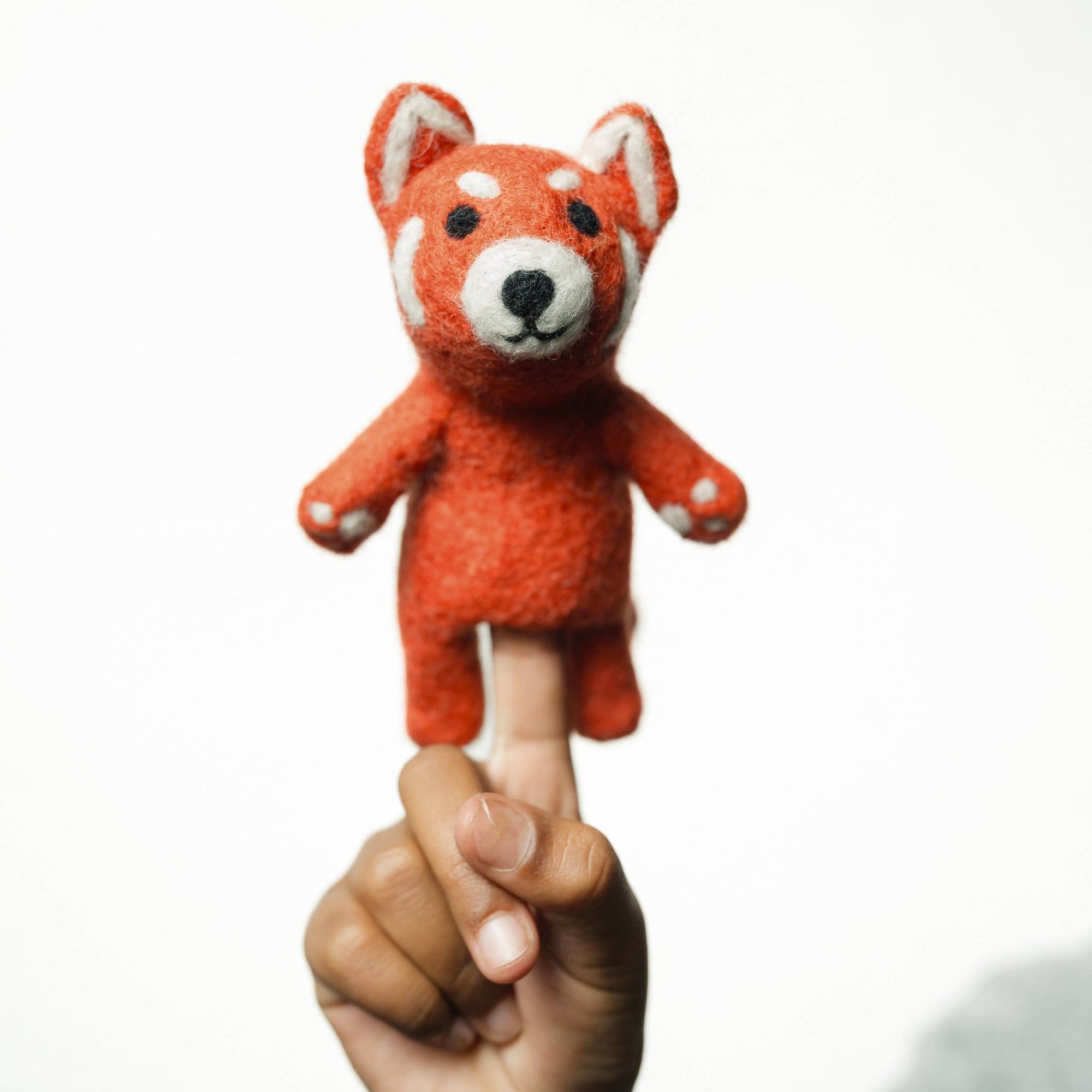 Hand holding a small orange fox plush finger puppet against a white background