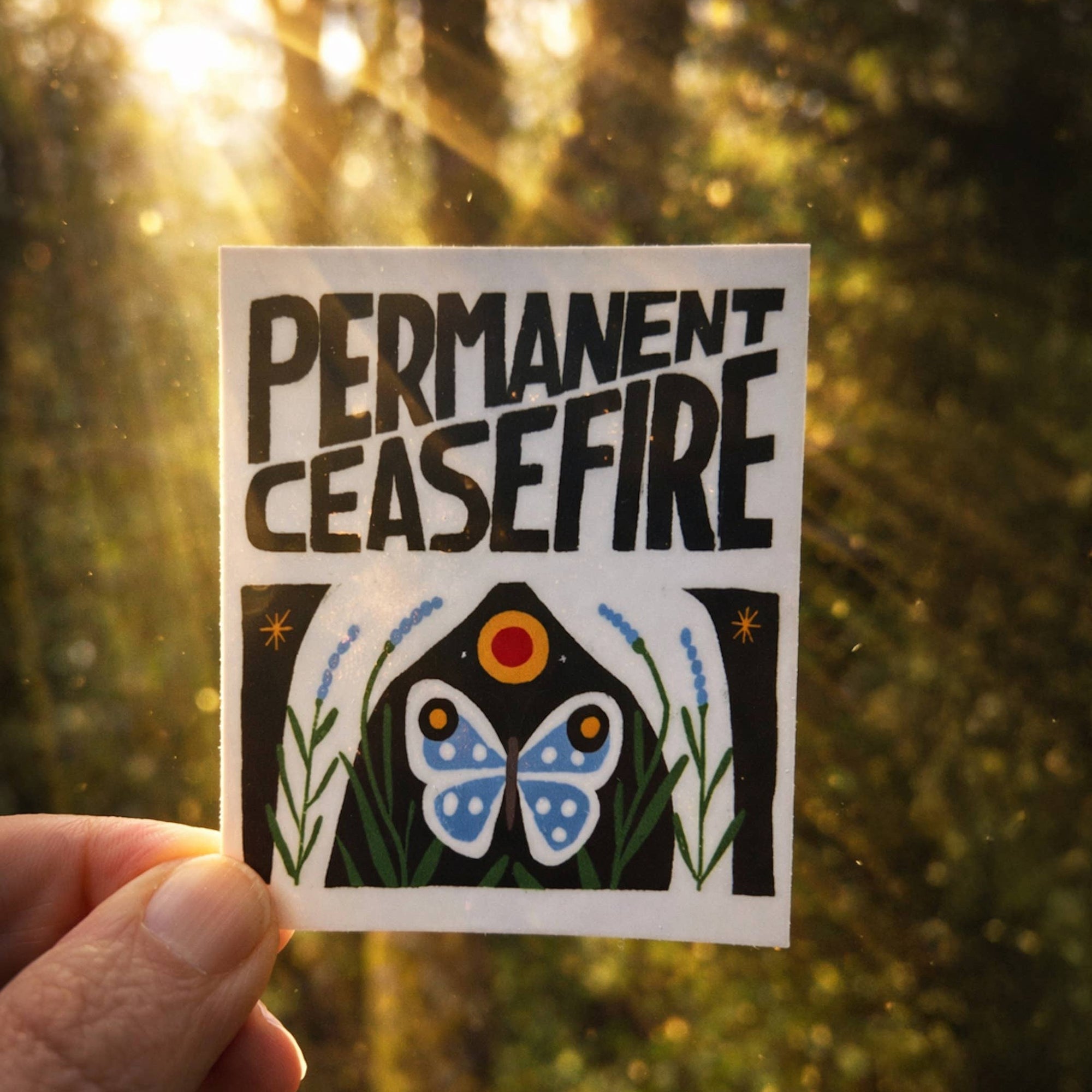 Sticker with 'Permanent Ceasefire' text held against a blurred natural background