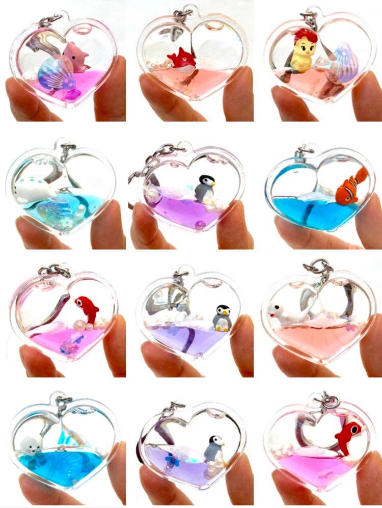 Heart-shaped keychains with various characters and scenes on a person's hand.