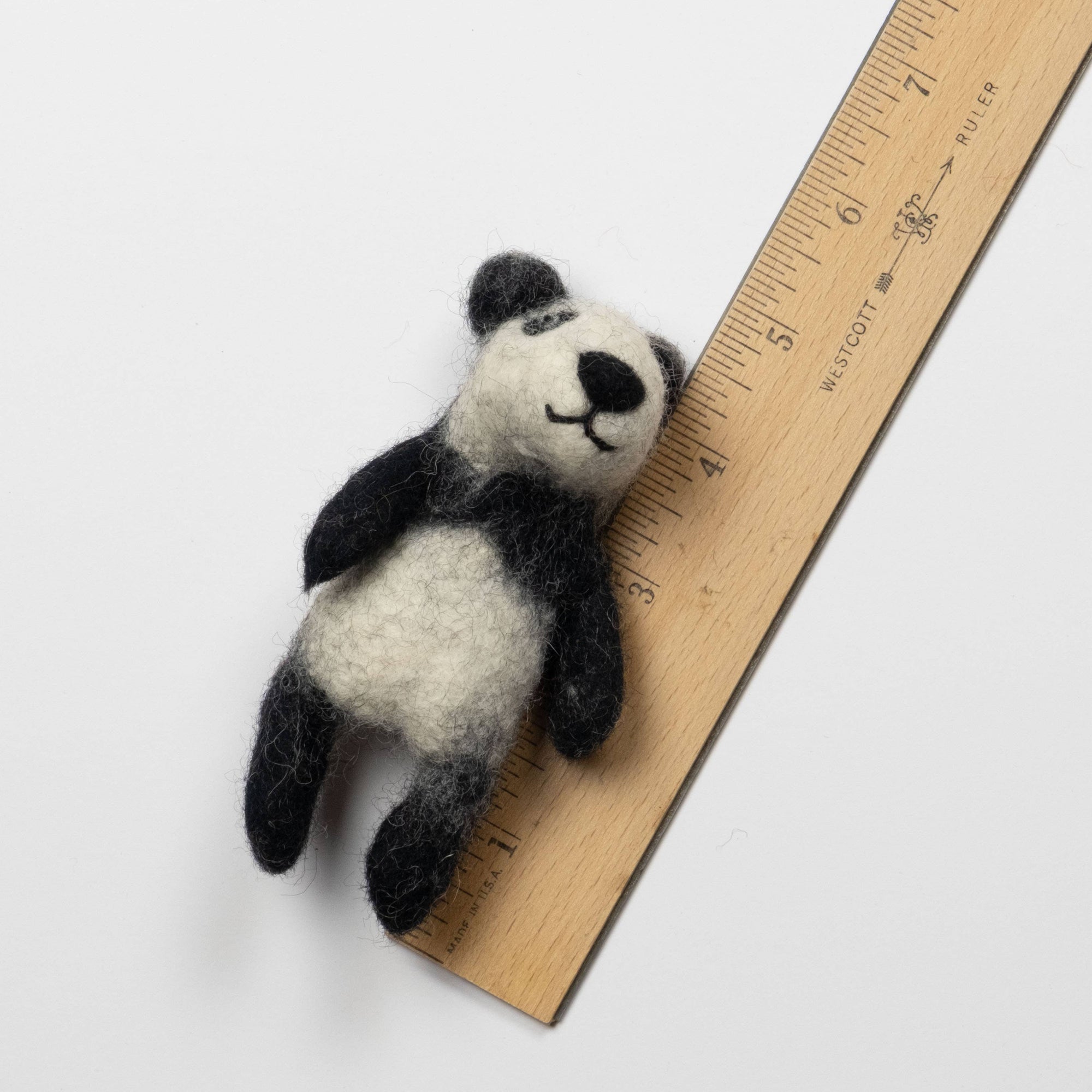 Small felt panda toy next to a wooden ruler on a white background