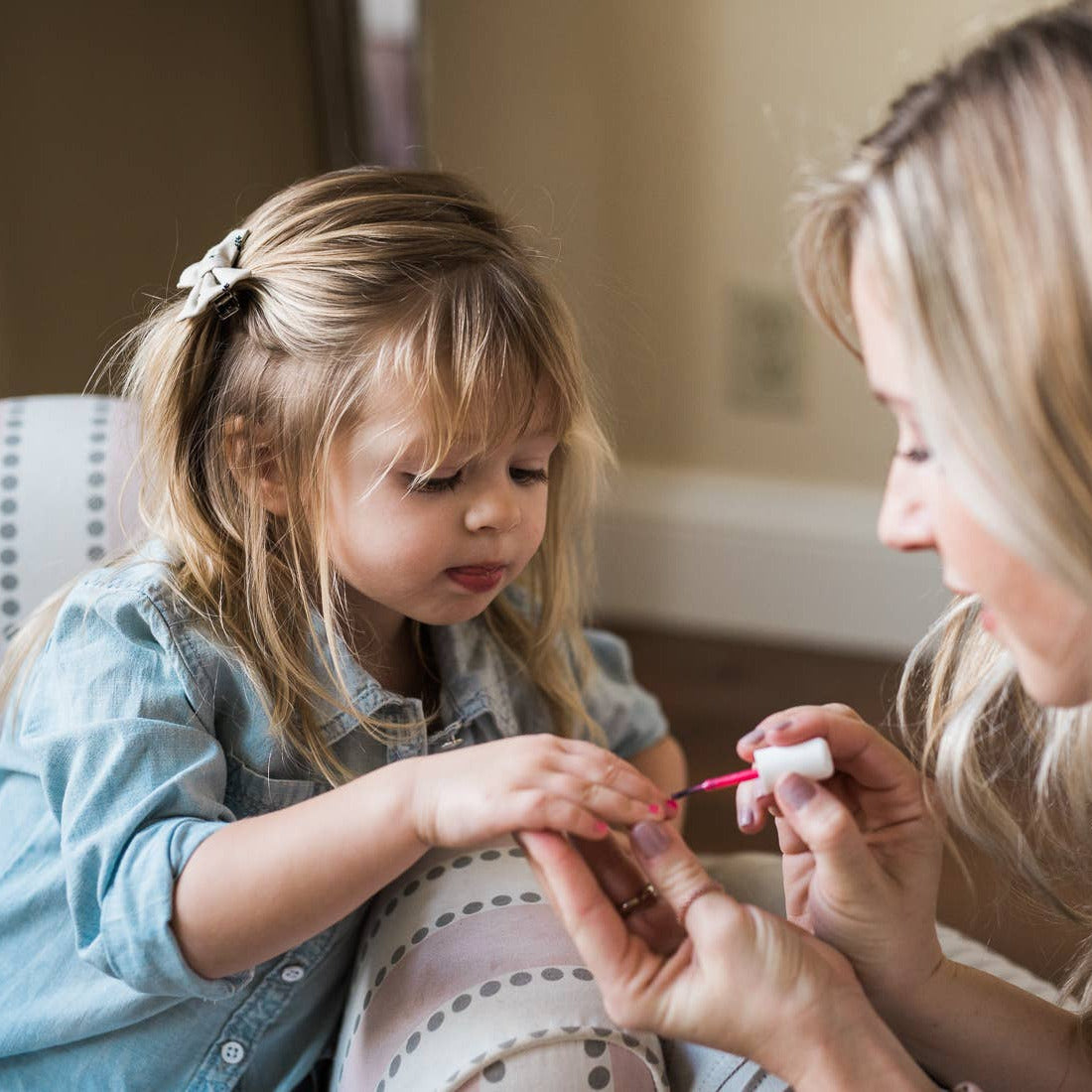 Woman applying nail polish to a child's fingernail in a home setting