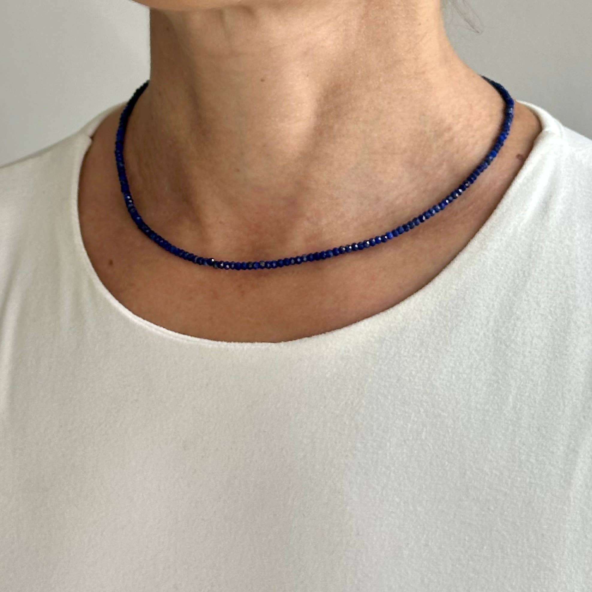 Person wearing a blue beaded necklace against a plain background