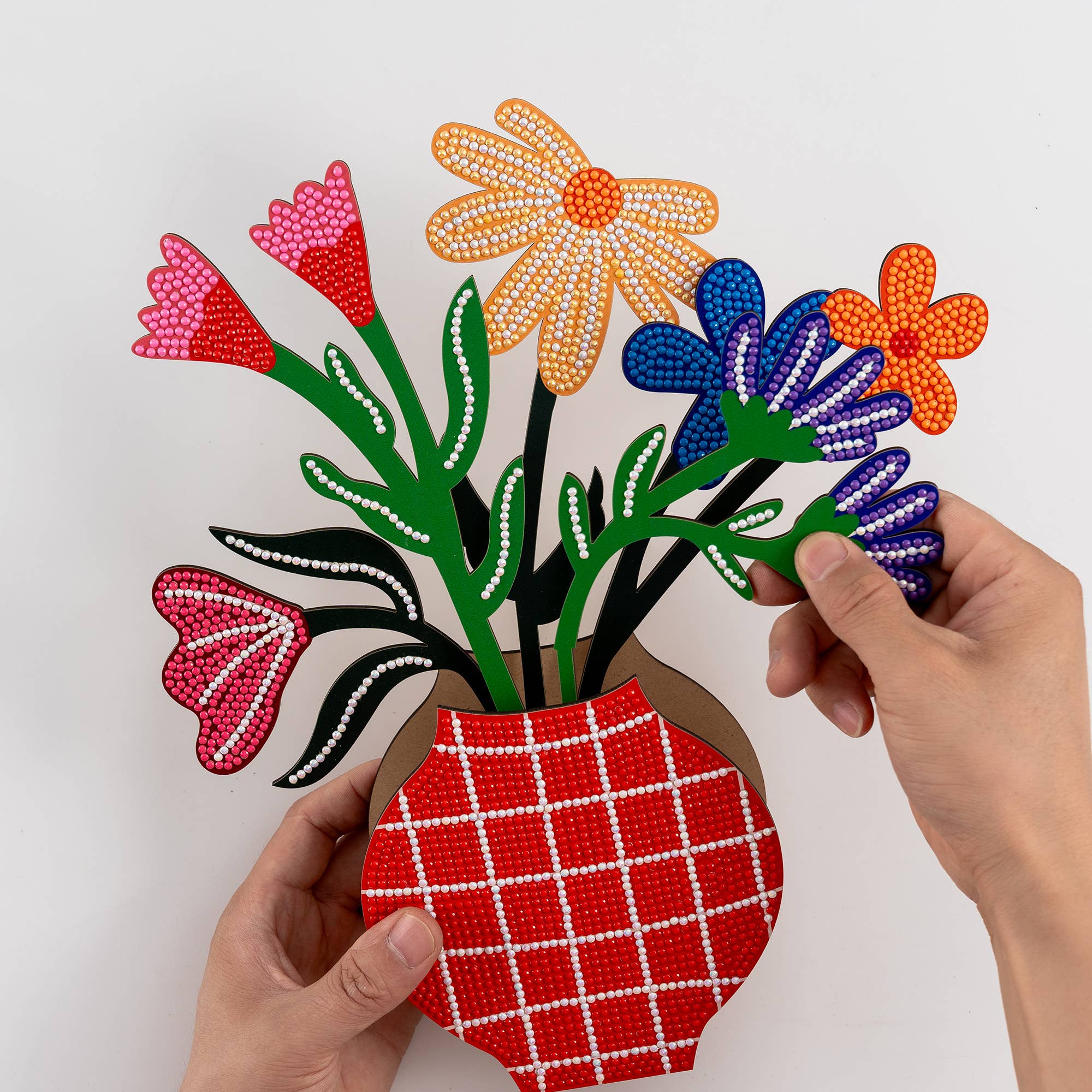 Colorful beaded flowers in a red vase held by hands against a white background