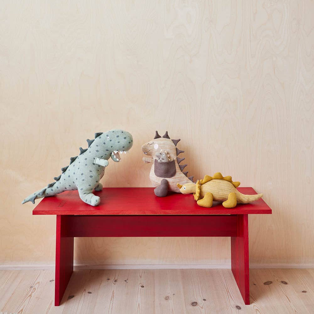 Three stuffed dinosaur toys on a red bench against a beige wall.